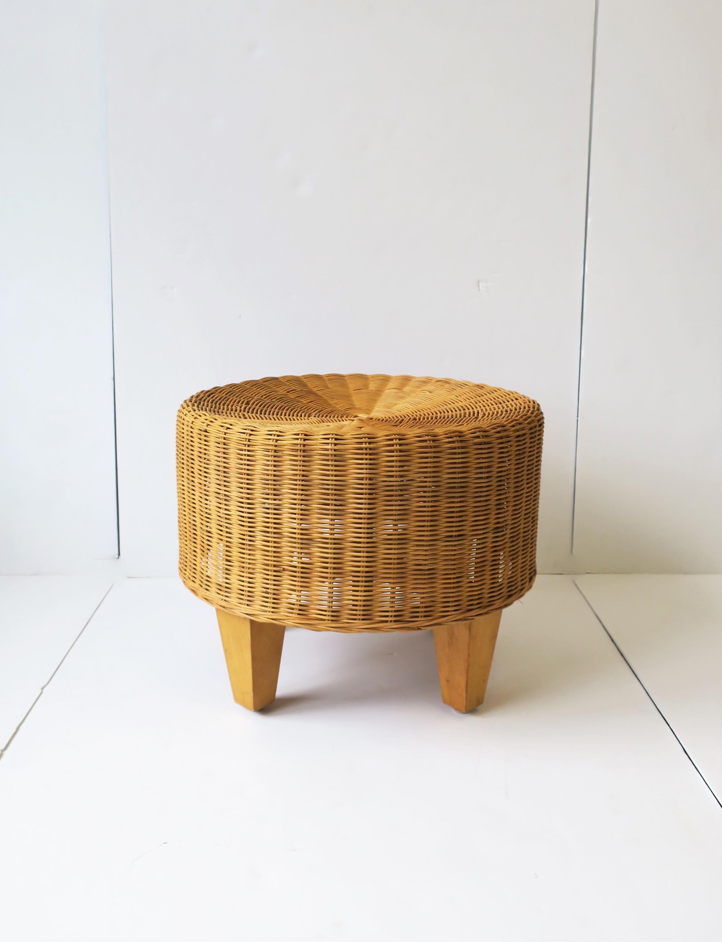 A round wicker stool or ottoman with tri-pod wood legs. Piece could also work as a side/drinks table providing there's a stable environment on top (e.g. coffee table book, as demonstrated.) Piece measures: 19