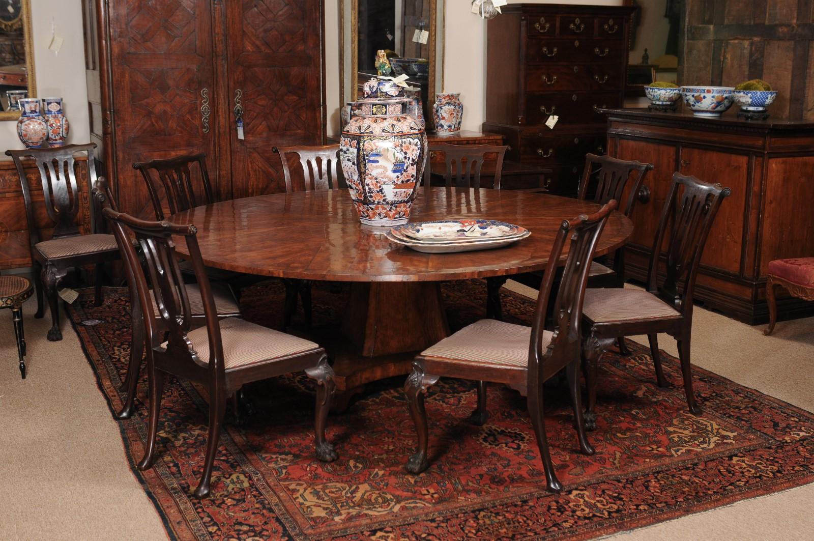 A round yew wood dining table featuring pedestal base and scroll feet. The table is a handmade reproduction possibly from England.
