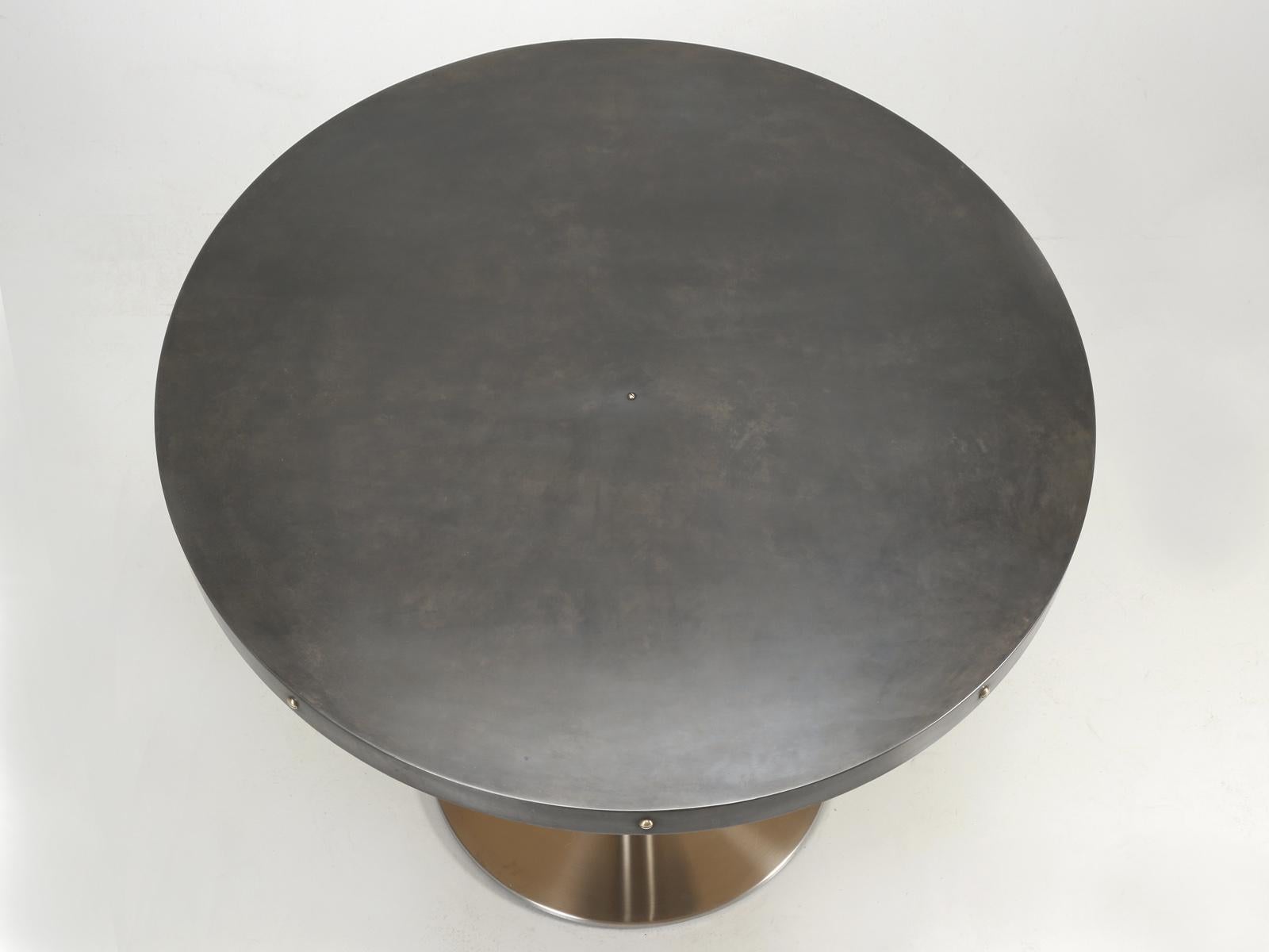 Round kitchen table, with a beautifully aged zinc top and an indestructible stainless-steel base. The zinc table is surrounded by solid brass slotted screws, which are both functional and add a bit of pop to the otherwise monochromatic scheme. 