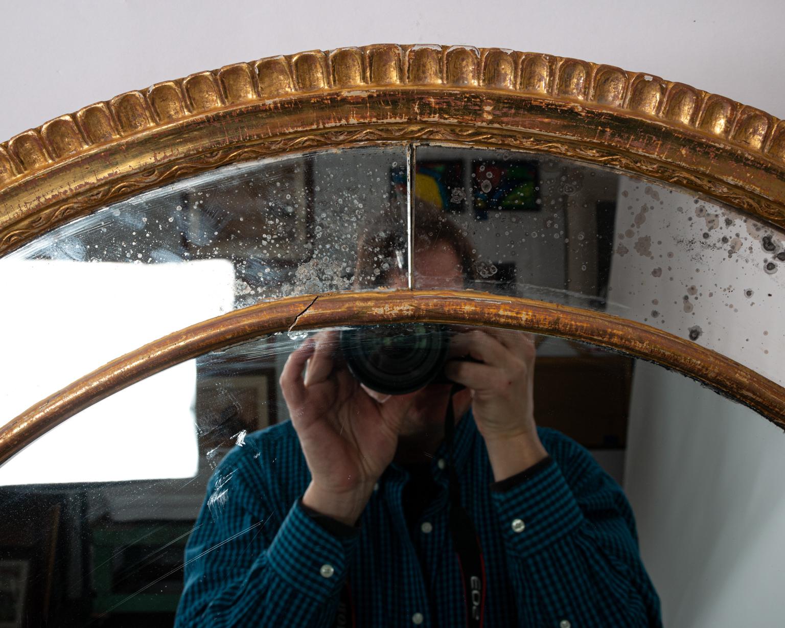 Rounded arch gilt mirror with smokey mirror insets and scalloped edges, circa 20th century. Please note of wear consistent with age and use including a crack in the mirror inset at the bottom along with oxidation. There is also some rubbing to the