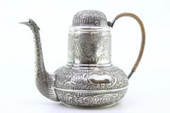 Rounded silver kettle w/ reliefs surrounding the monogram card & coated handle