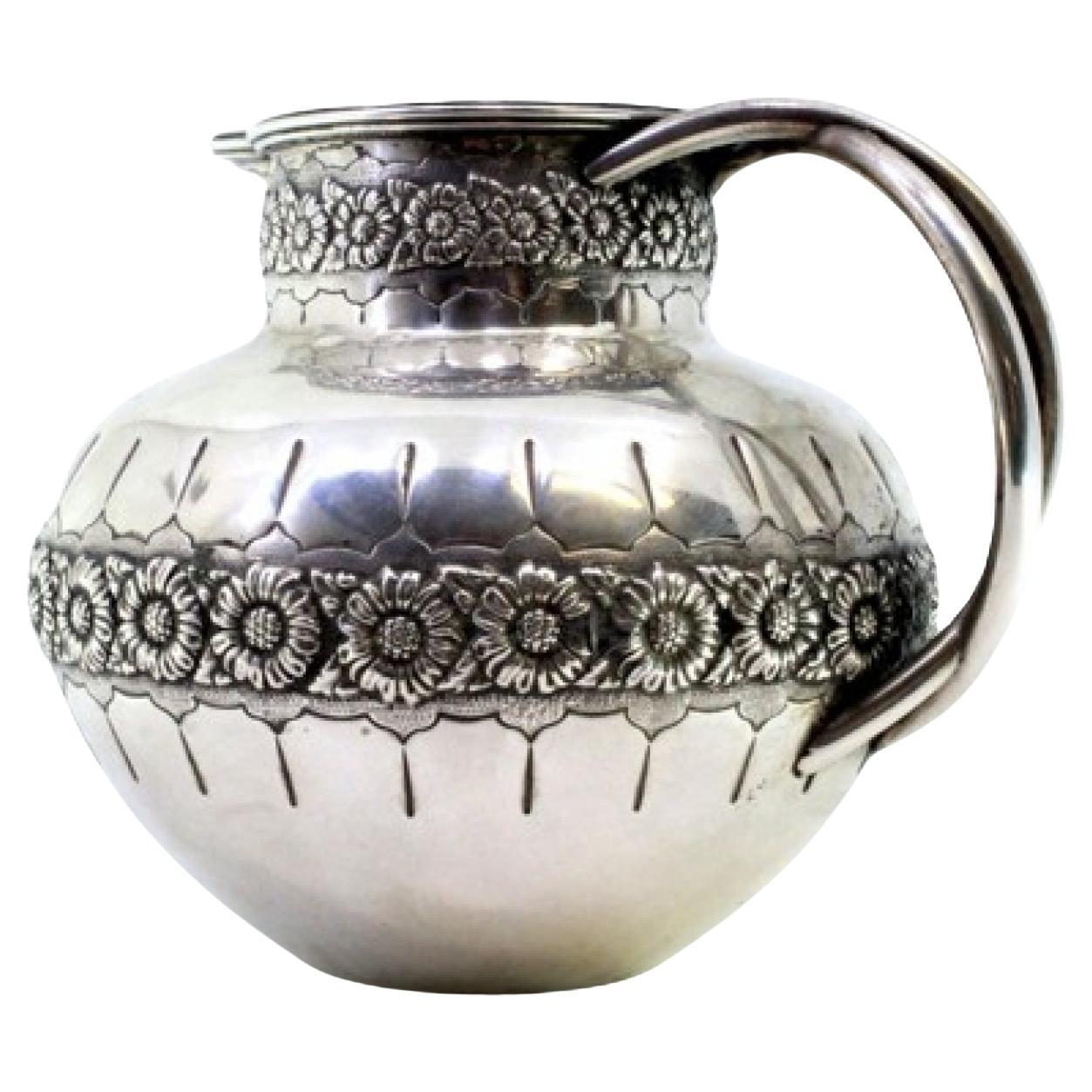 Rounded silver wine jug with exposed floral motifs, double handle and beaded rim