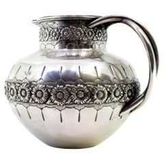 Rounded silver wine jug with exposed floral motifs, double handle and beaded rim