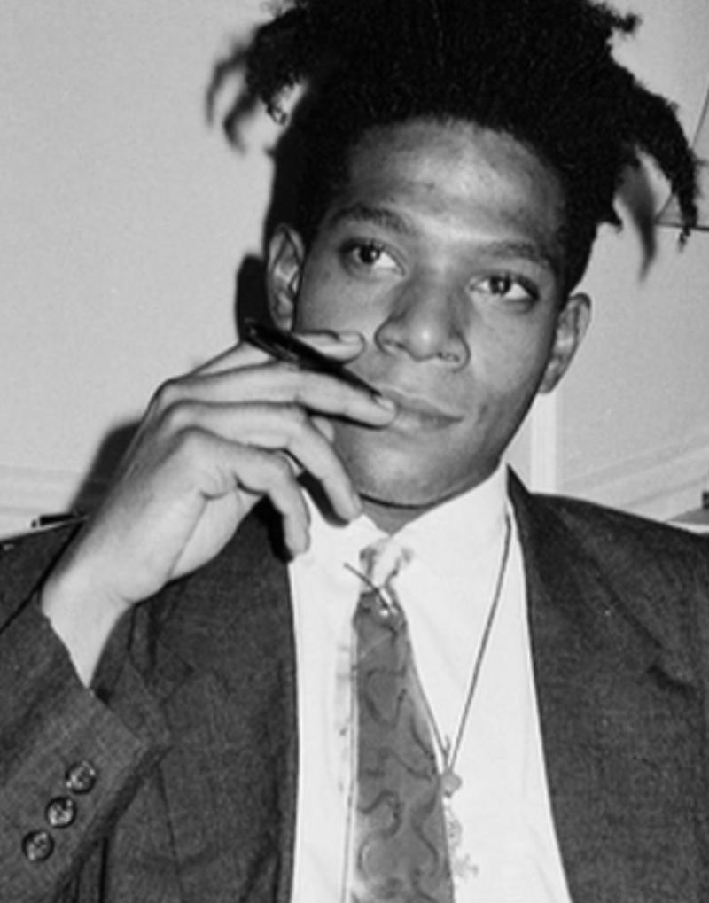 Ritratto in bianco e nero del giovane artista Jean-Michel Basquiat in completo, seduto a un tavolo, fotografato da Roxanne Lowit nel 1985.

Tutte le stampe sono in edizione limitata. Disponibile in più misure. Cornici di alto livello su