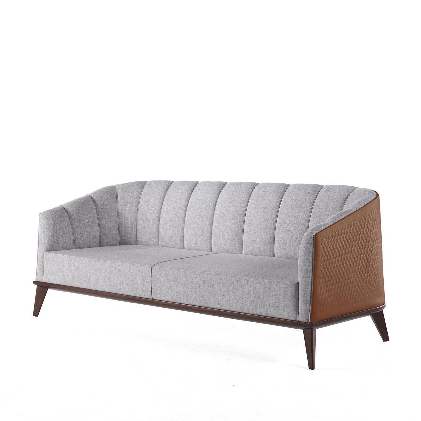 The Roy Sofa showcases gentle curves and a plush silhouette entirely upholstered in an elegant heather gray fabric. The wraparound back and sloping arms, detailed with wide, vertical channels, form a shape that perfectly encompasses both comfort and