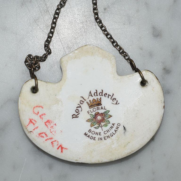 A small ceramic decanter or liquor bottle scotch tag. A wonderful way to add interest to your bar, this piece features a ceramic medallion that hangs from a metal chain. The front of the label reads 