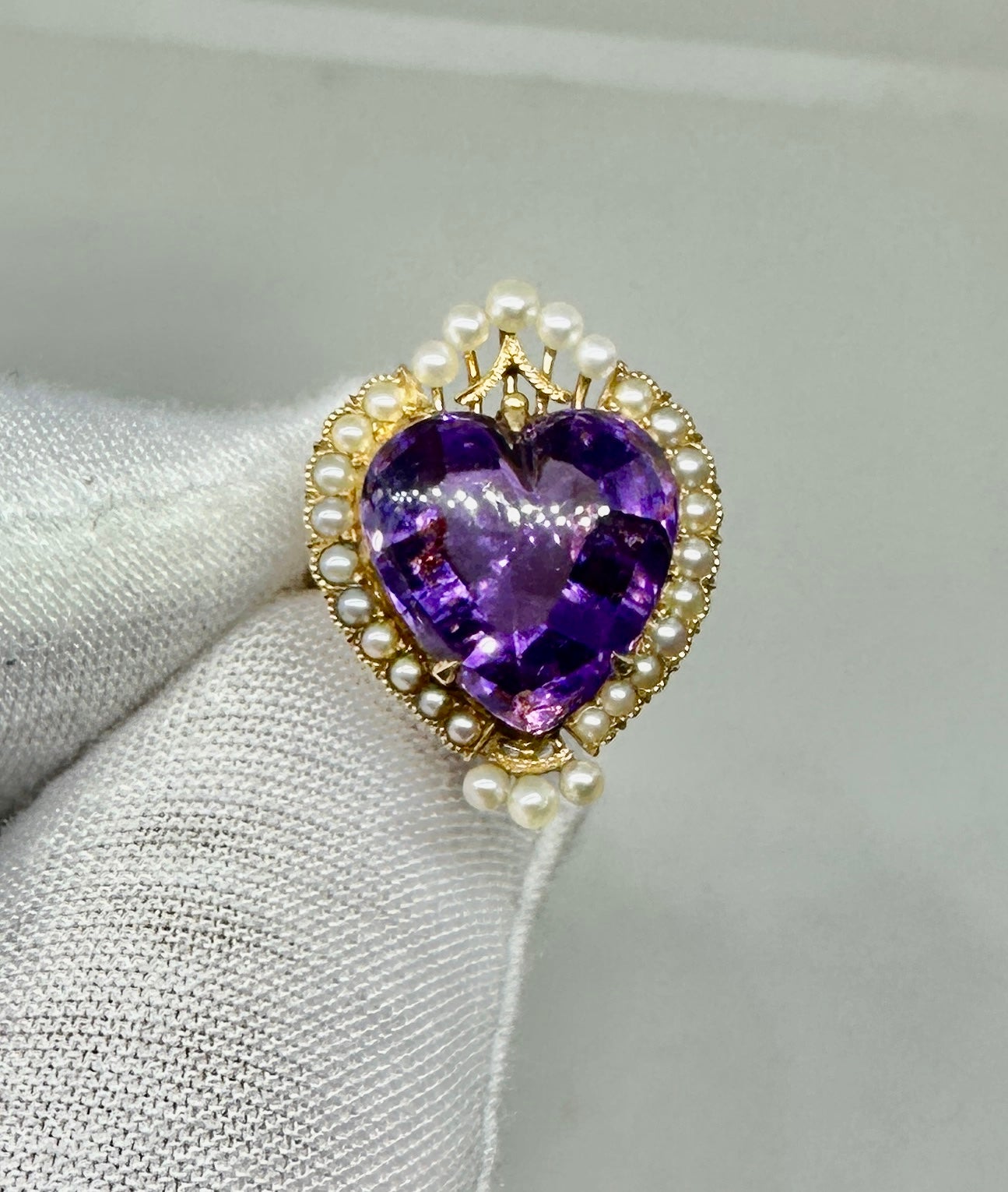 This is a magnificent antique ring with a gorgeous Heart Shape Royal Amethyst with a Pearl crown and halo in 14 Karat Gold.
The central Royal Amethyst is a stunning heart shape gem that has been carved by one of the finest lapidary artisans. The