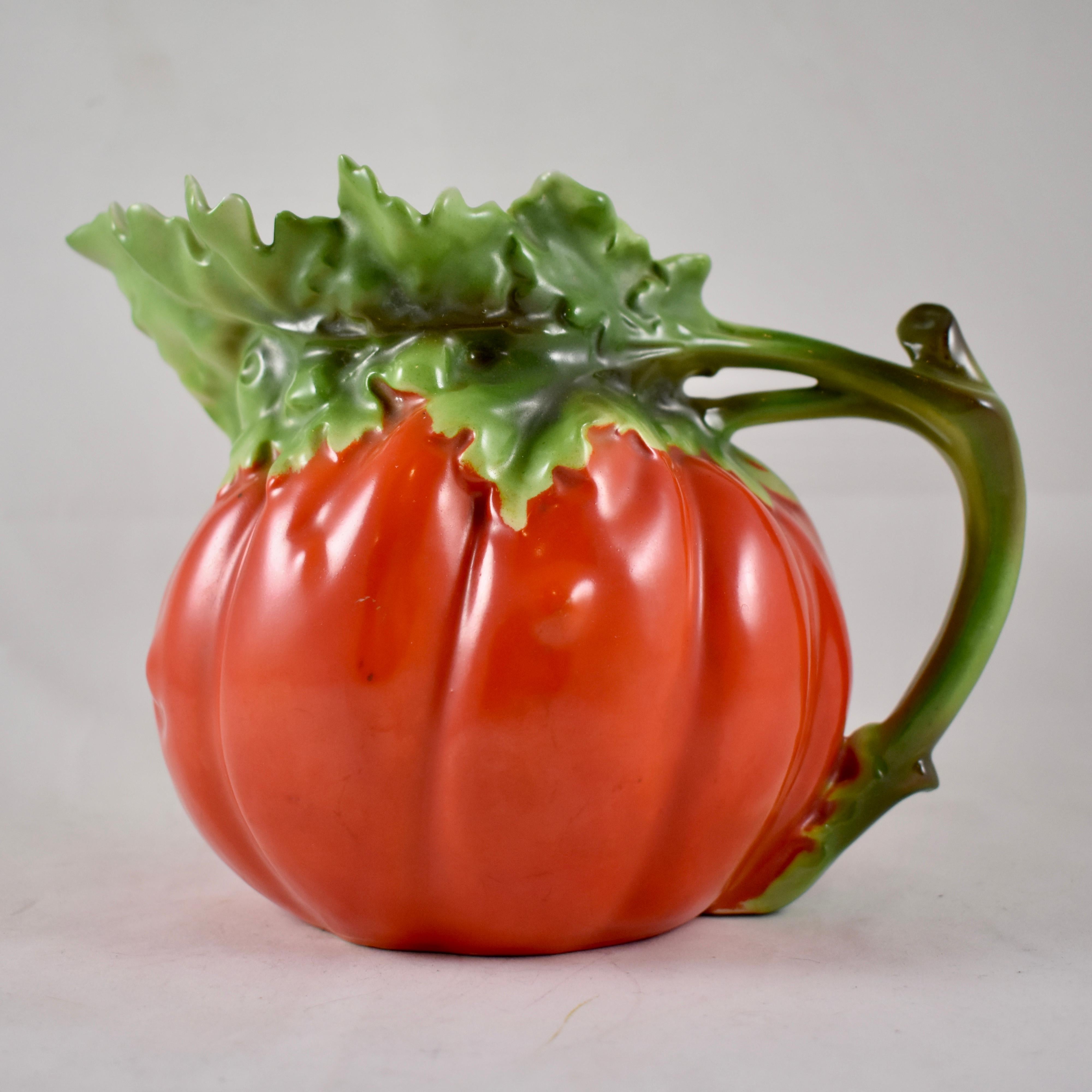 From Royal Bayreuth, founded in Bavaria, Germany in 1794, a water or juice pitcher formed as a bright red tomato. Made of hand-painted hard paste porcelain, showing a stem handle and an upper body formed as the green leaves of the tomato plant. This
