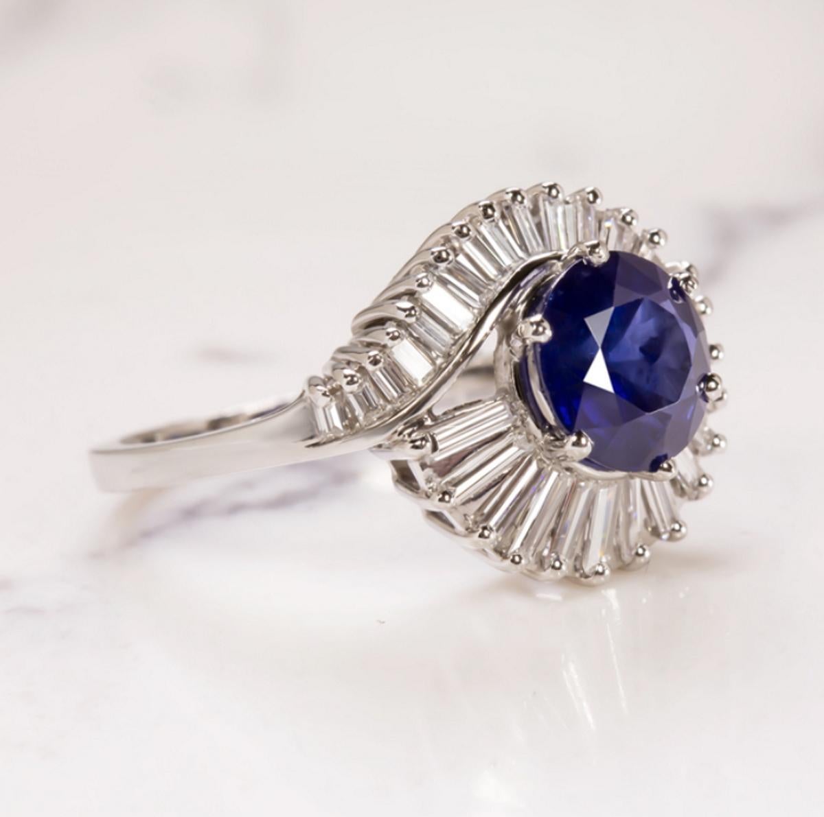 This eye-catching and high quality sapphire and diamond ring truly brings the glamour and the sparkle! The substantial 2.40ct round cut sapphire center is surrounded by a shimmering halo of high quality baguette cut diamonds. The sapphire has