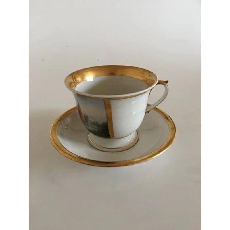 Royal Copenhagen antique morning cup and saucer with handpainted motif of Frederiksborg Castle.

The motif is intact and the gold looks nice with only some minor wear. The handle has a reparation and a hairline. The cup is 9 cm height (3 35/64