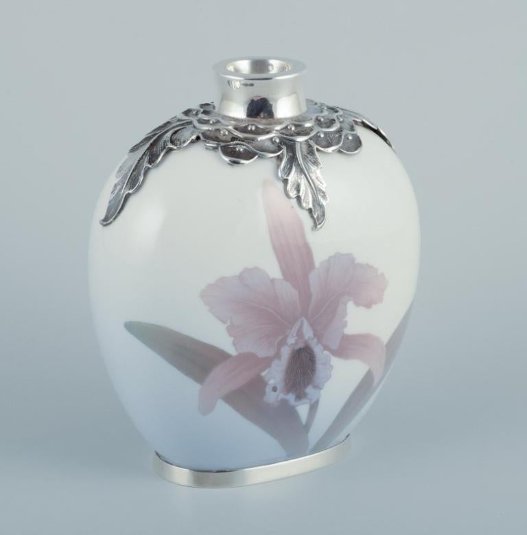 Royal Copenhagen, vaso Art Nouveau in porcellana con intarsi in argento sterling nella parte superiore e inferiore. Motivo floreale sottosmalto. 
Punzoni d'argento del 1912. 
Seconda qualità di fabbrica. 
Contrassegnato. 
In ottime condizioni.
