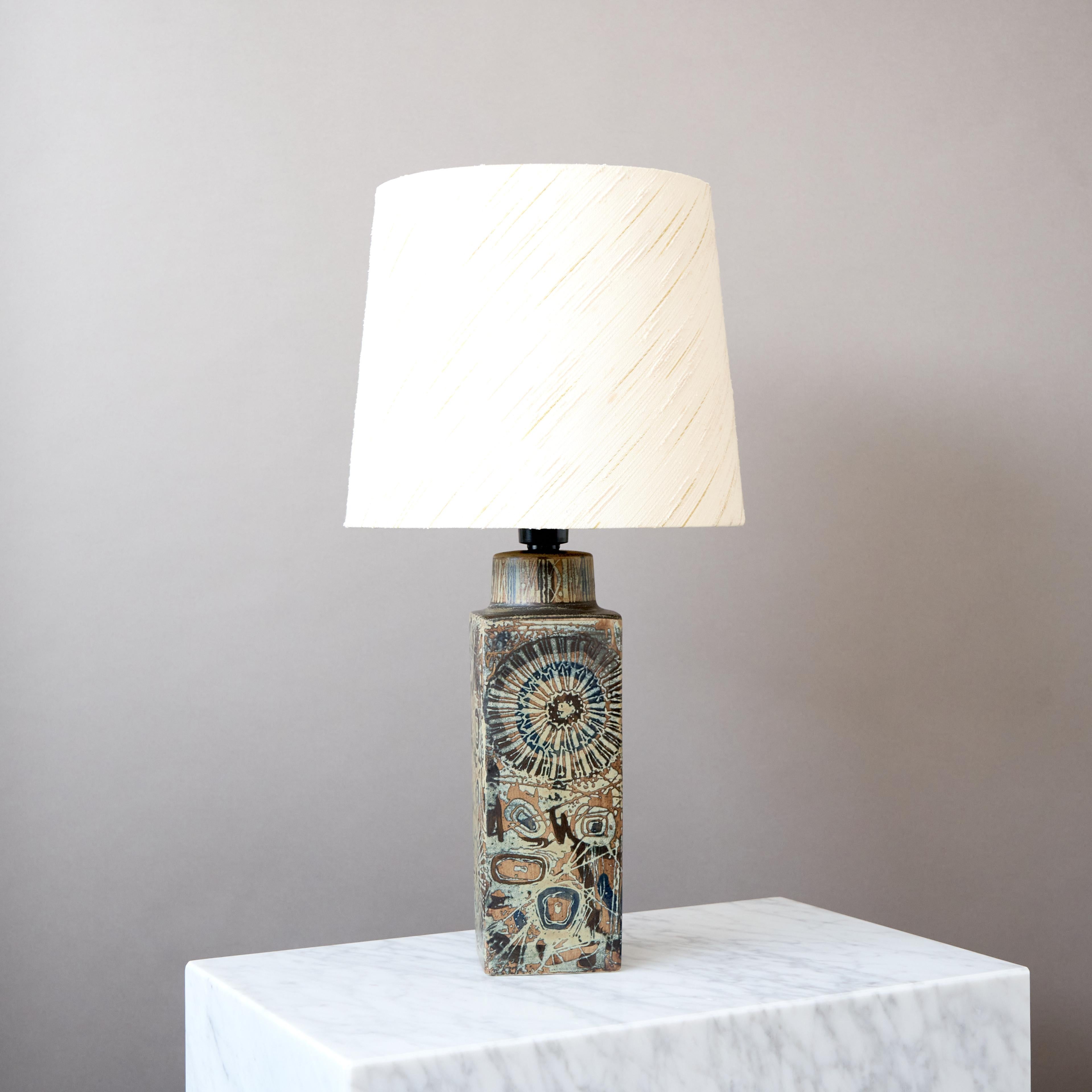 Lámpara de sobremesa de cerámica diseñada por Nils Thorsson para Royal Copenhagen y Fog & Mørup y fabricada hacia la década de 1970.

Presenta una decoración floral abstracta en esmalte mate marrón y azul. El surafaz es táctil.

La lámpara es una
