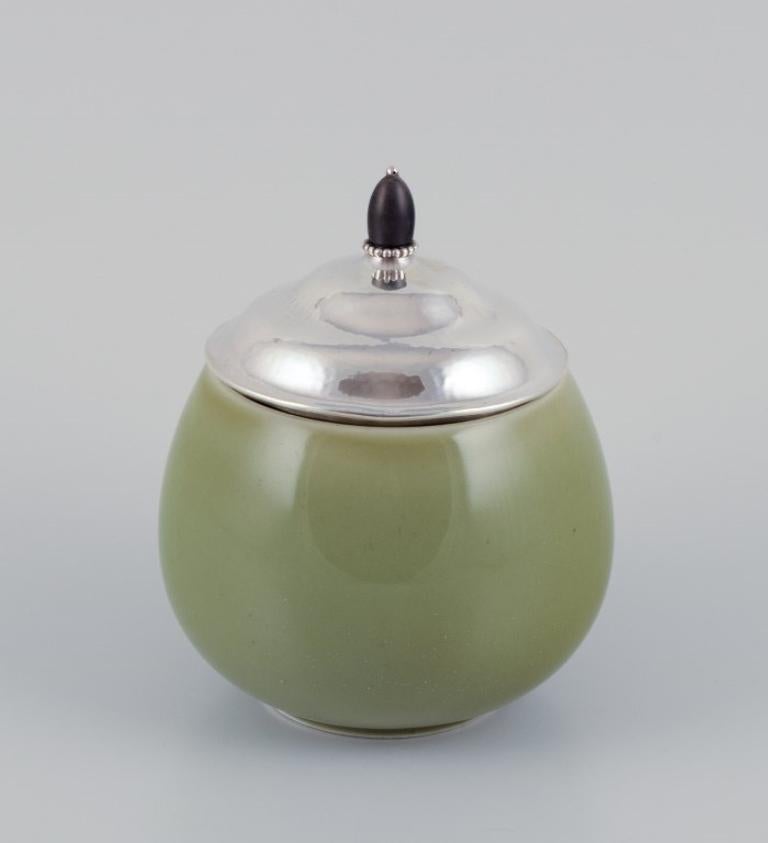 Royal Copenhagen ceramic jar. Silver lid with an ebony knob.
Celadon glaze.
Model 20610.
Dating: 1957.
The jar is marked. The silver lid is likely from Georg Jensen, unmarked.
In perfect condition.
First factory quality.
Dimensions: D 13.0 cm x H