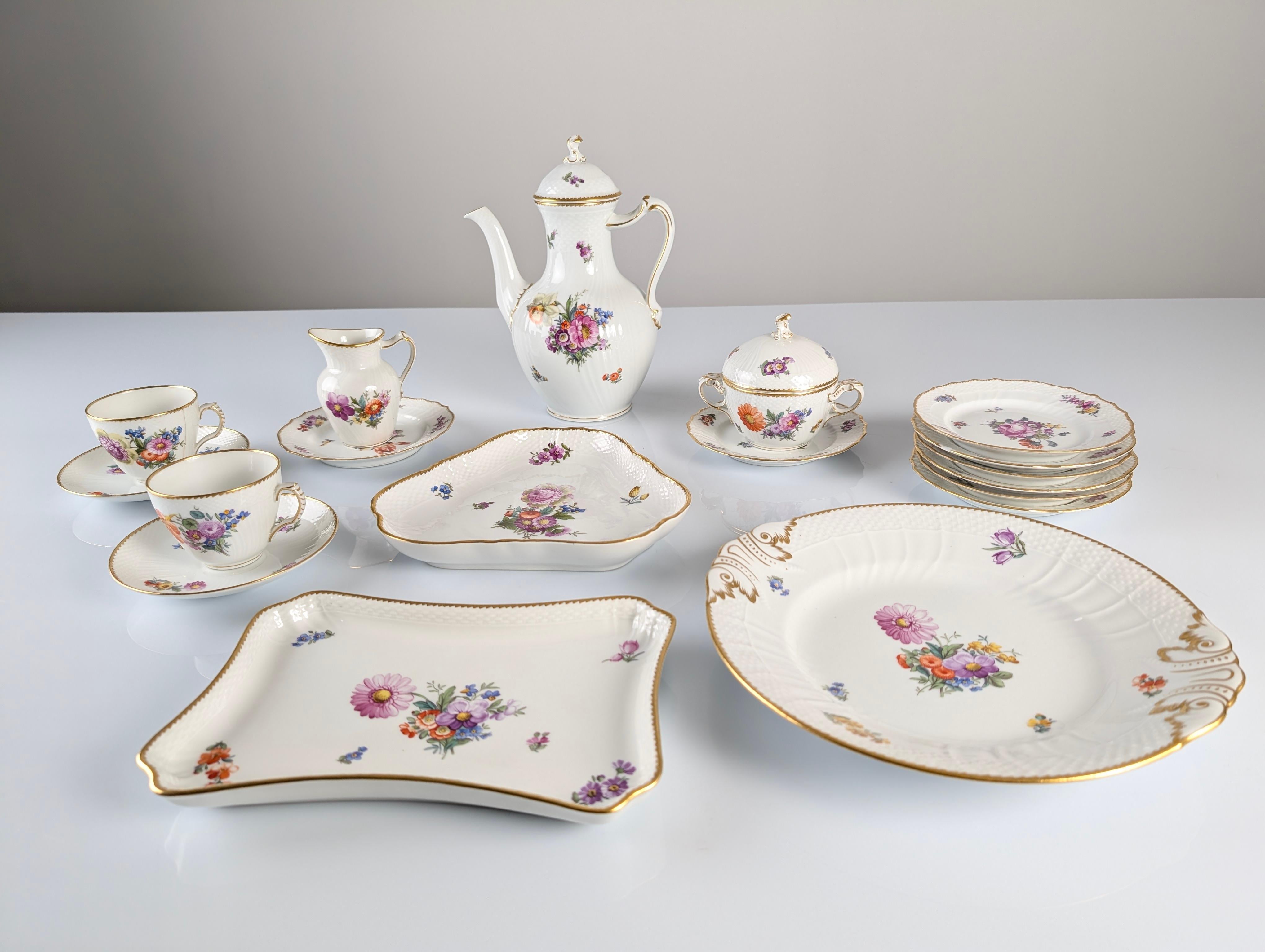Questo squisito set da tè/caffè di Royal Copenhagen, collezione Saxon Flower, è un esempio eccezionale del miglior artigianato europeo. Ogni pezzo è decorato a mano con delicati motivi floreali policromi, arricchiti da dettagli dorati dipinti con