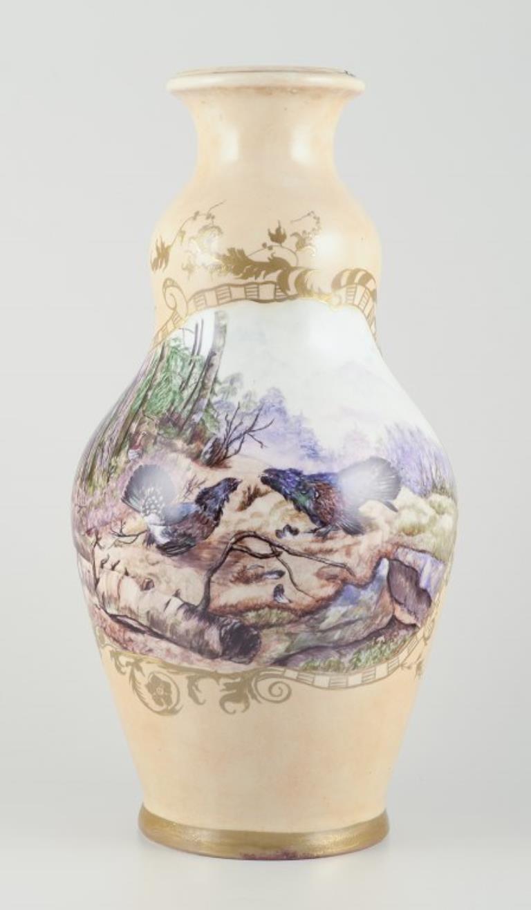 Royal Copenhagen. Colossal porcelain vase.
Motif of two wood grouses (Tetrao urogallus) in a forest landscape, gold decoration.
Hand-painted in overglaze technique. 
Marked with Juliane Marie stamp and an indistinct artist signature. Also 