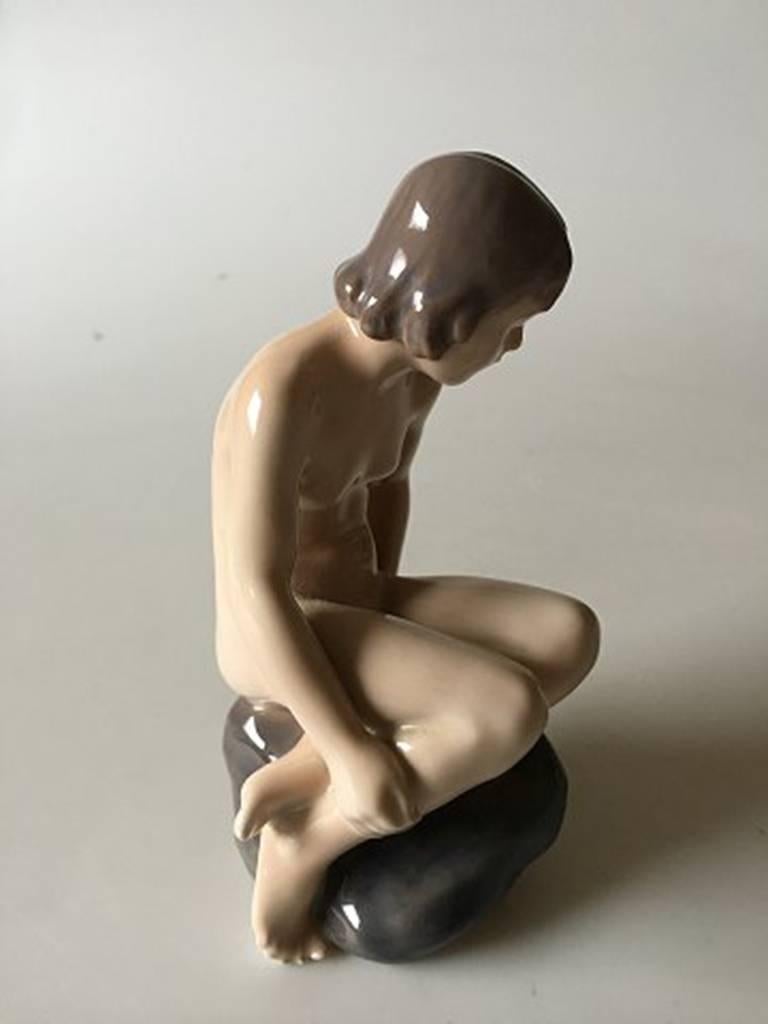 Royal Copenhagen figurine girl on stone #4027. Measures 15 cm and is in good condition. Designed by Ada Bonfils.