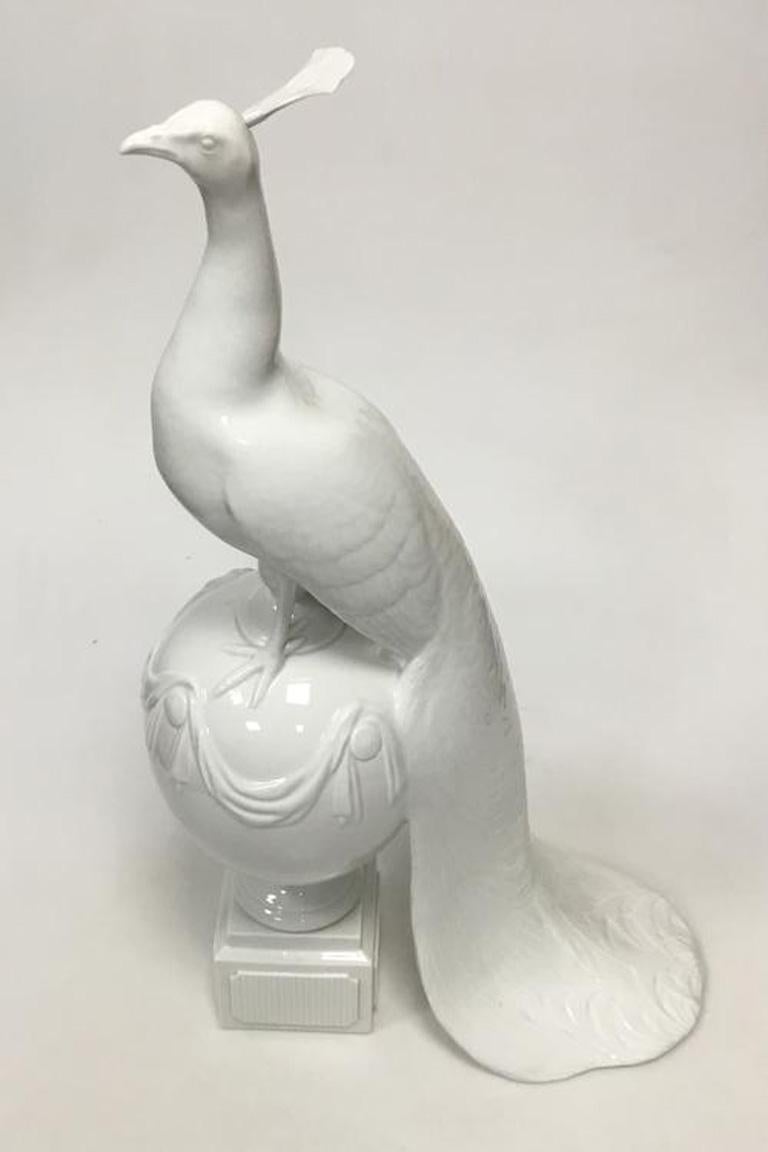 Royal Copenhagen figurine of peacock on ball. 

Designed by Arnold Krog. 

Measures 55 cm (21 21/32 in.). 

2nd grade and the figure has a skew. 

Hair splendor is loosely applied.