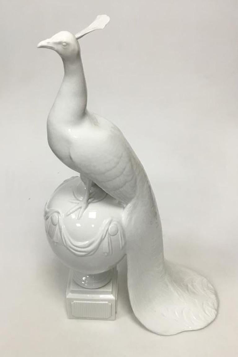Royal Copenhagen figurine of peacock on ball. 

Designed by Arnold Krog. 

Measures 55 cm (21 21/32 in.). 

2nd grade and the figure has a skew. 

Hair splendor is loosely applied.