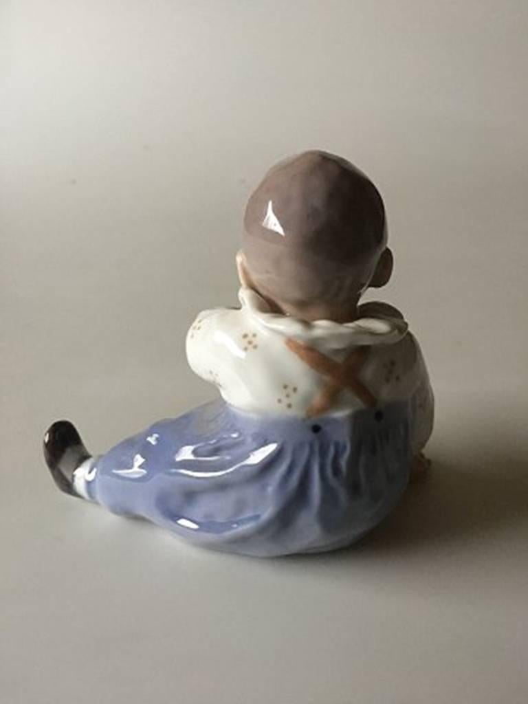 Figurine Royal Copenhagen Enfant assis No 1517. Mesure 9 cm / 3 35/64 in. x 11 cm / 4 21/64 in. et est en bon état. Conçu par Else Sandholt.