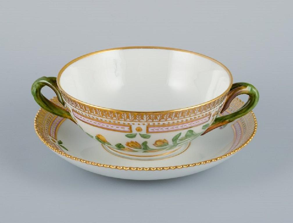 Royal Copenhagen Flora Danica bouillon cup with saucer in hand painted porcelain with branch-shaped handles, flowers and gold decoration. 
PROVENANCE: VALDEMARS CASTLE
Model number 20/3612. 
Cup dimensions: 13 x 5,5 cm.
Saucer diameter: 17