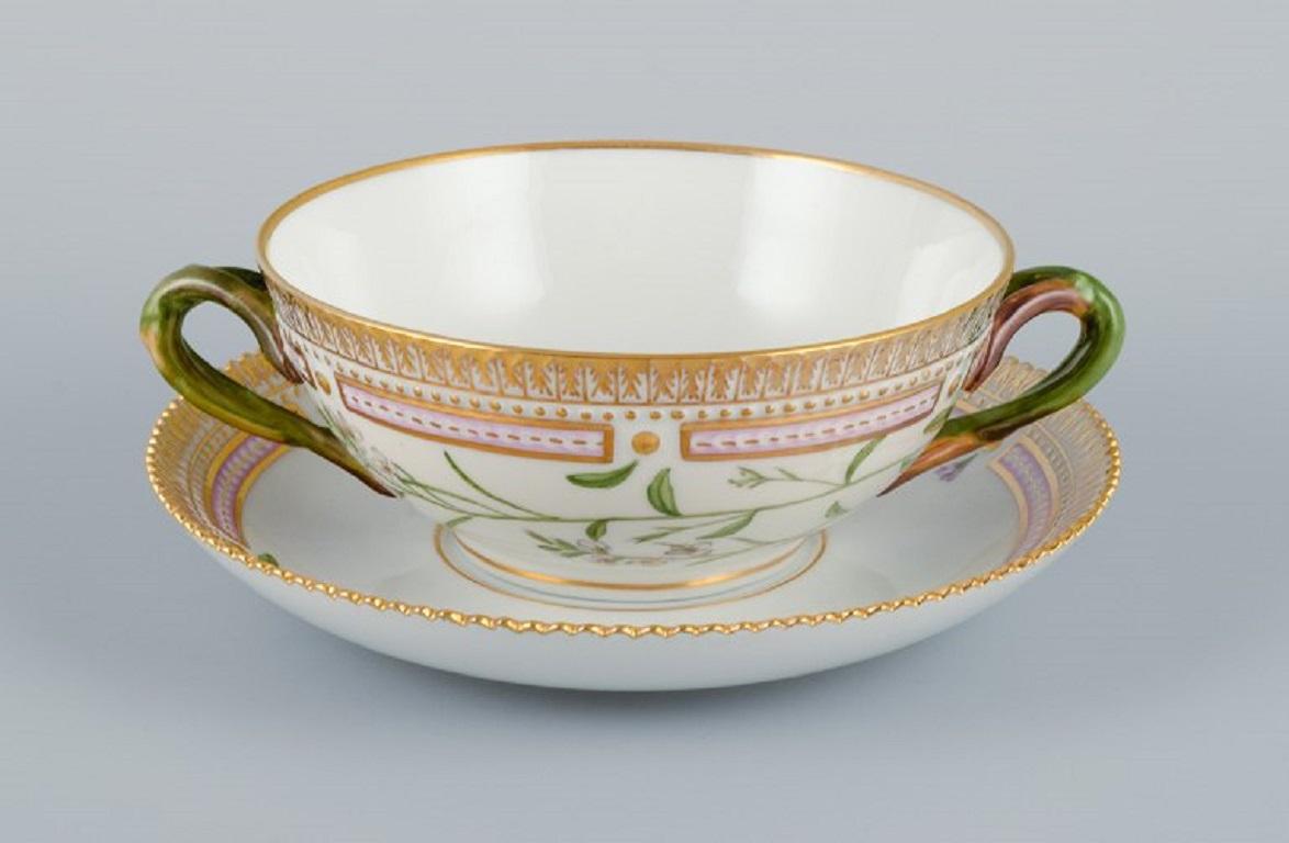 Royal Copenhagen Flora Danica bouillon cup with saucer in hand painted porcelain with branch-shaped handles, flowers and gold decoration. 
PROVENANCE: VALDEMARS CASTLE
Model number 20/3612. 
Cup dimensions: 13 x 5,5 cm.
Saucer diameter: 17