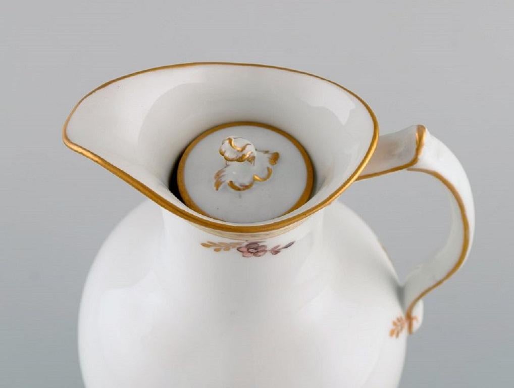 Royal Copenhagen Golden Basket chocolate jug in porcelain with flowers and gold decoration. 
Model number 595/9424. Early 20th century.
Measures: 23 x 16 cm.
In excellent condition.
Stamped.
1st factory quality.