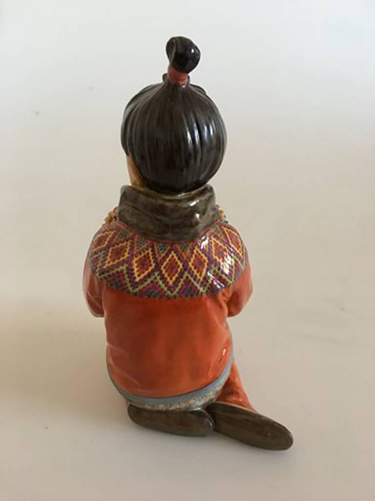 Royal Copenhagen over-glaze figurine Greenland girl #12415. Measures: 15cm and is in good condition, but has chip on flower. Designed by Carl Martin-Hansen.