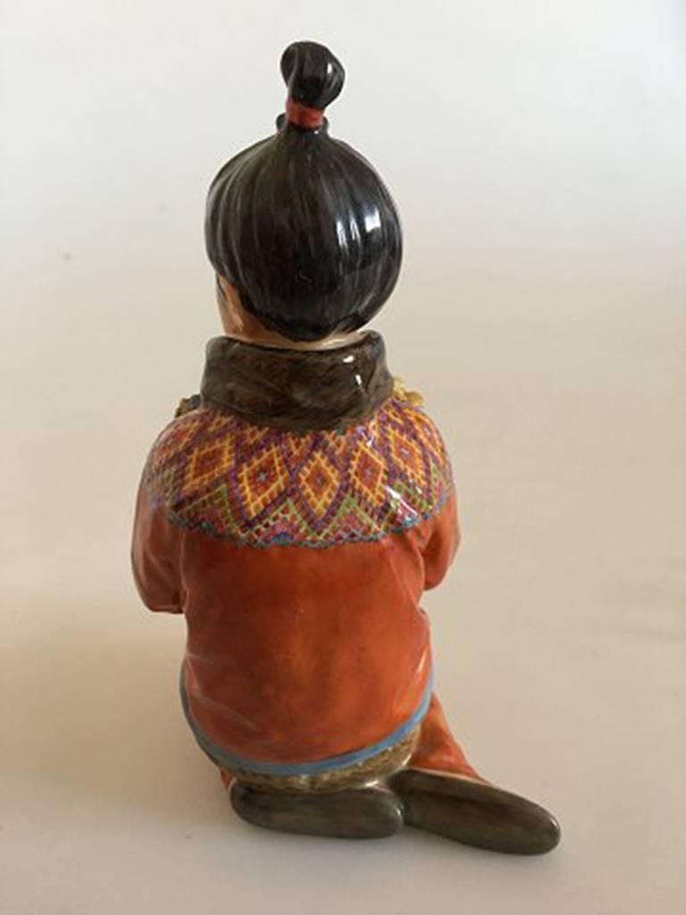Royal Copenhagen over-glaze figurine Greenland girl #12415. Measures: 15cm and is in good condition, but has chip on flower. Designed by Carl Martin-Hansen.
