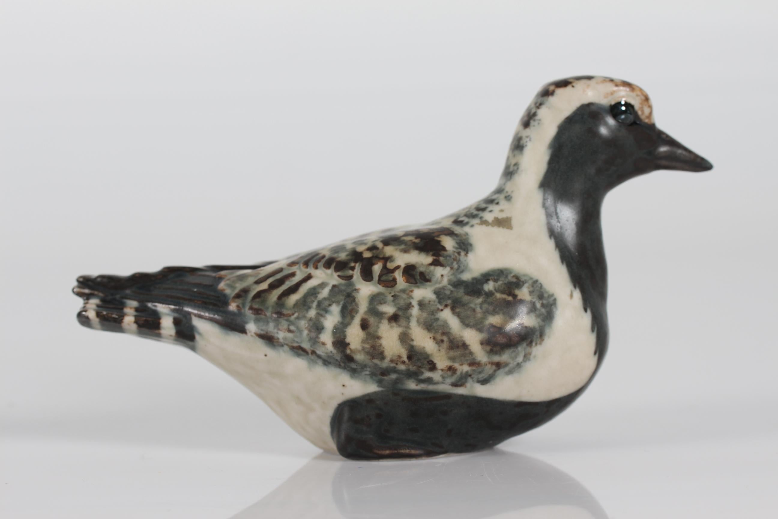 Stoneware figurine of the golden plover model no. 22486 designed by Jeanne Grut and manufactured by Royal Copenhagen
The bird is decorated with glaze in white, grey and black colors
Stamp mark from the 1970s

Measures: Height 10 cm
Length 18