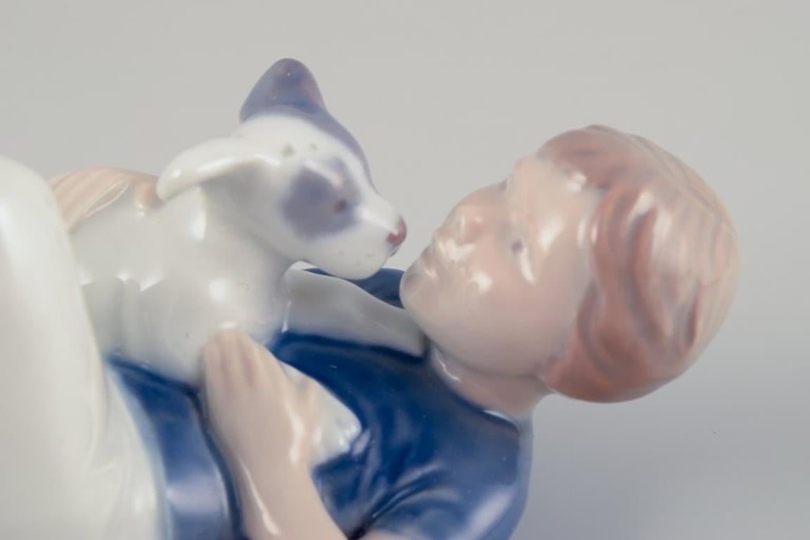 Smaltato Royal Copenhagen. Statuetta in porcellana di un ragazzo con un cucciolo. Rara statuetta. in vendita