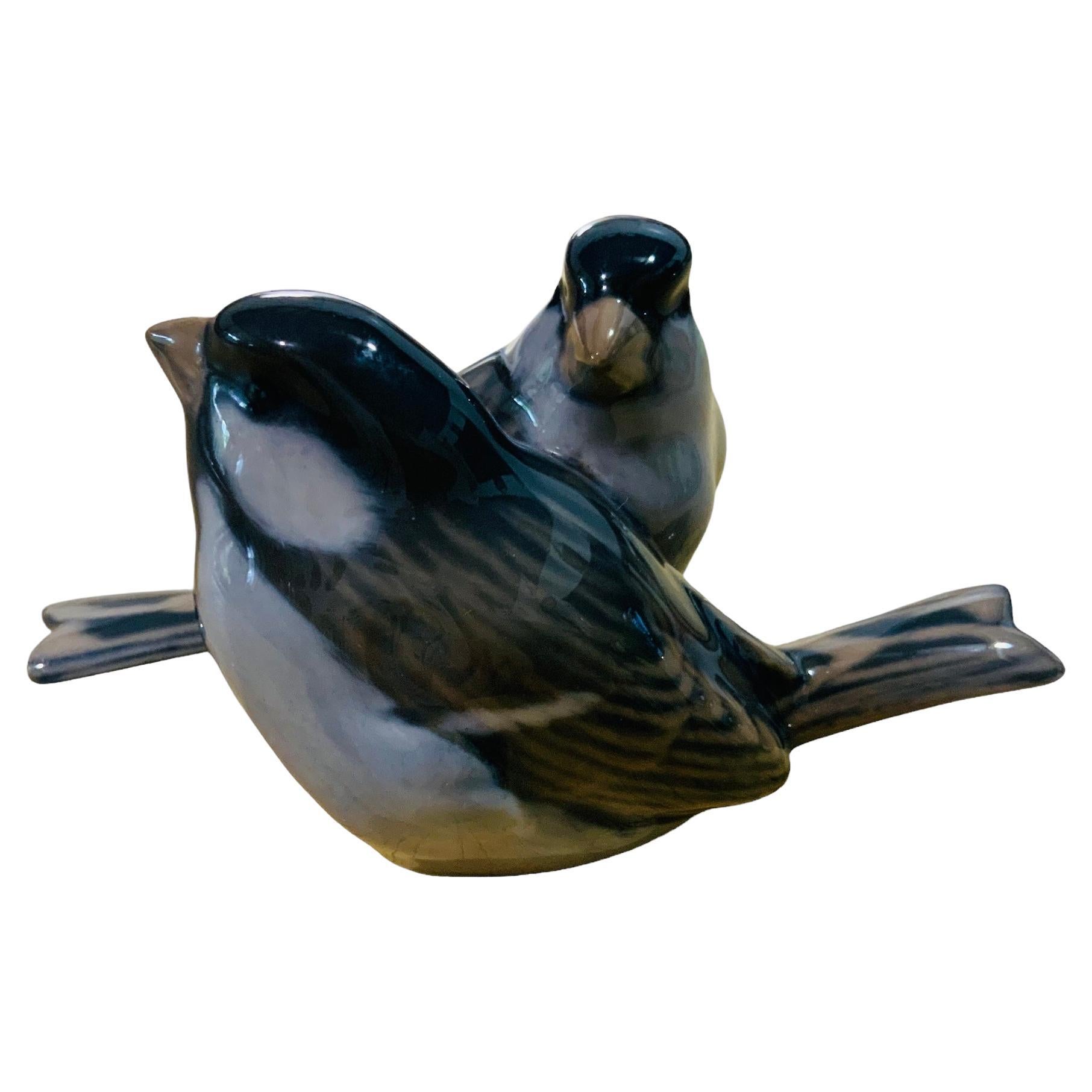This is a Royal Copenhagen porcelain of a pair of small plump and feathery birds figurines known as sparrows. At the base is the Royal Copenhagen hallmark with the number-1309, a crown and Denmark. It is hand painted white, light brown, blue and