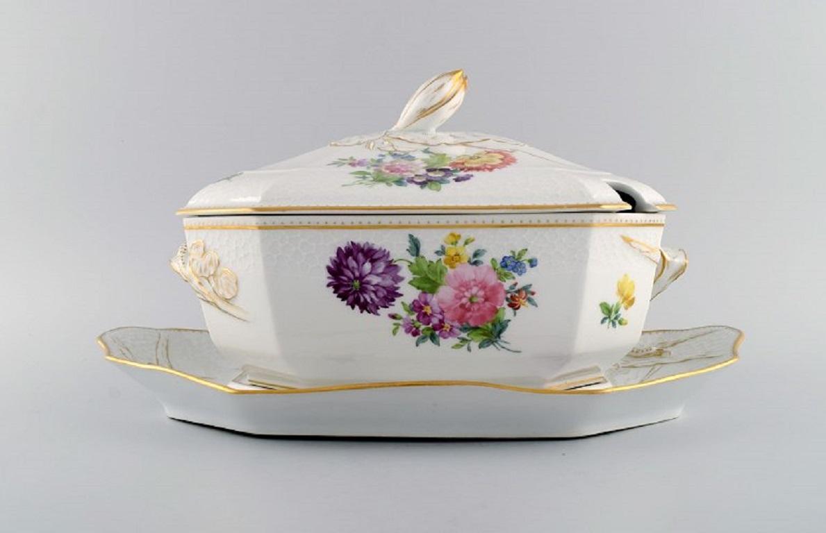 Royal Copenhagen Saxon Flower special version. 
Large and rare lidded tureen with saucer. Lid and handles modelled as foliage. 
Hand-painted flowers and gold decoration. Approx. 1900.
The tureen measures: 31 x 21 x 21 cm.
Saucer measures: 39 x