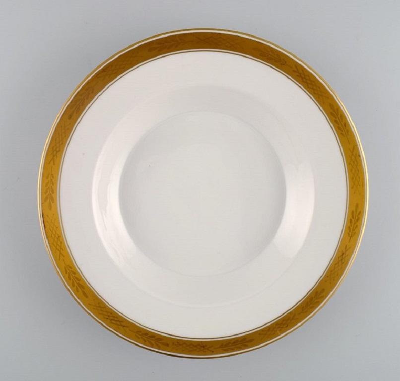 Royal Copenhagen service no. 607. 
Twelve deep porcelain plates. Gold border with foliage. 
Model number 607/9587. 
Dated 1944.
Measures: 25 x 4 cm.
In excellent condition.
Stamped.
1st factory quality.