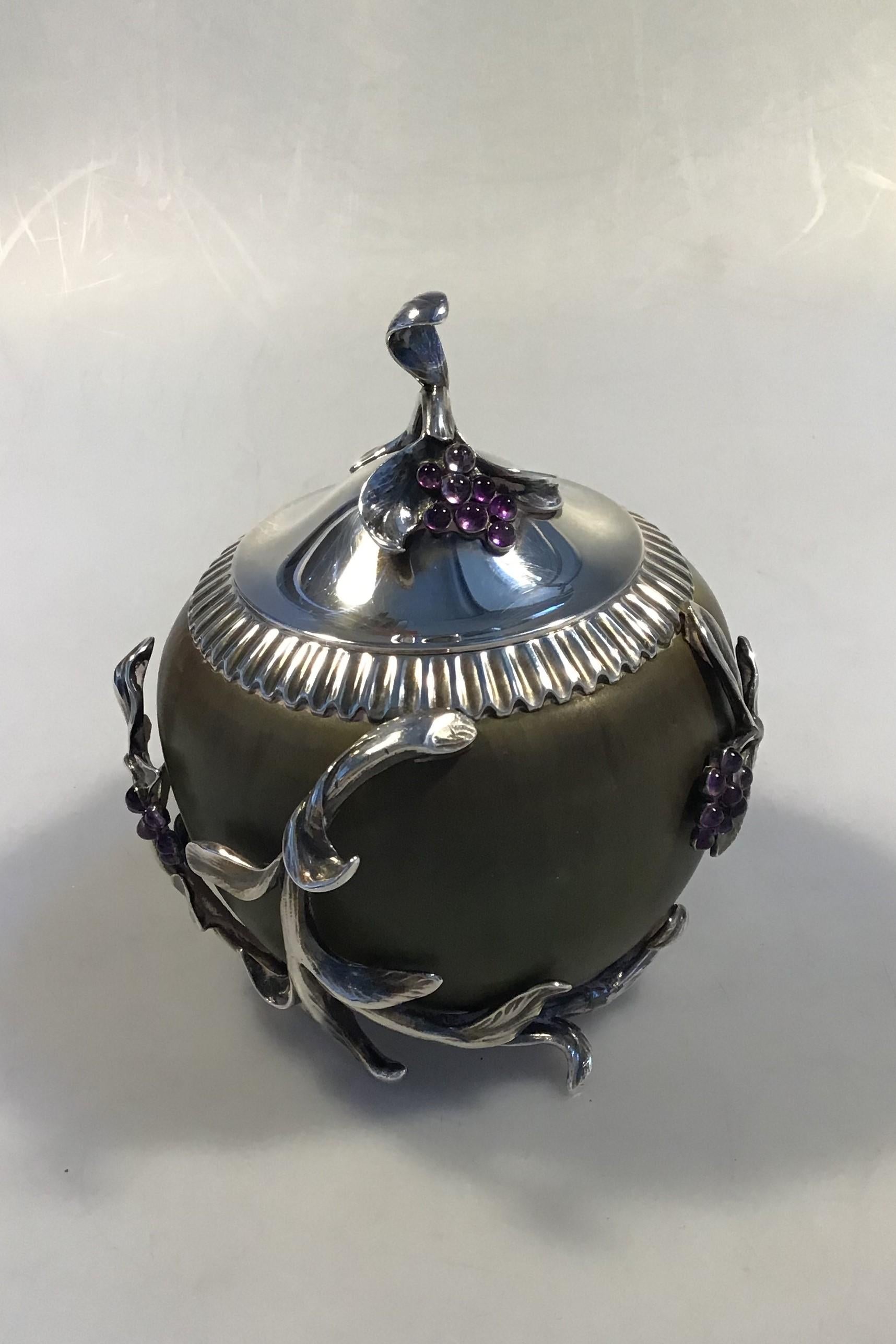 Royal Copenhagen (Patrick Nordstrøm). Jar in stoneware with green Sung glaze, Anton Michelsen mounting with lid in sterling silver with leaves and grape bunches of a total of 30 amethysts. Signed PN, with three waves and dated 5/12 1919. Silver