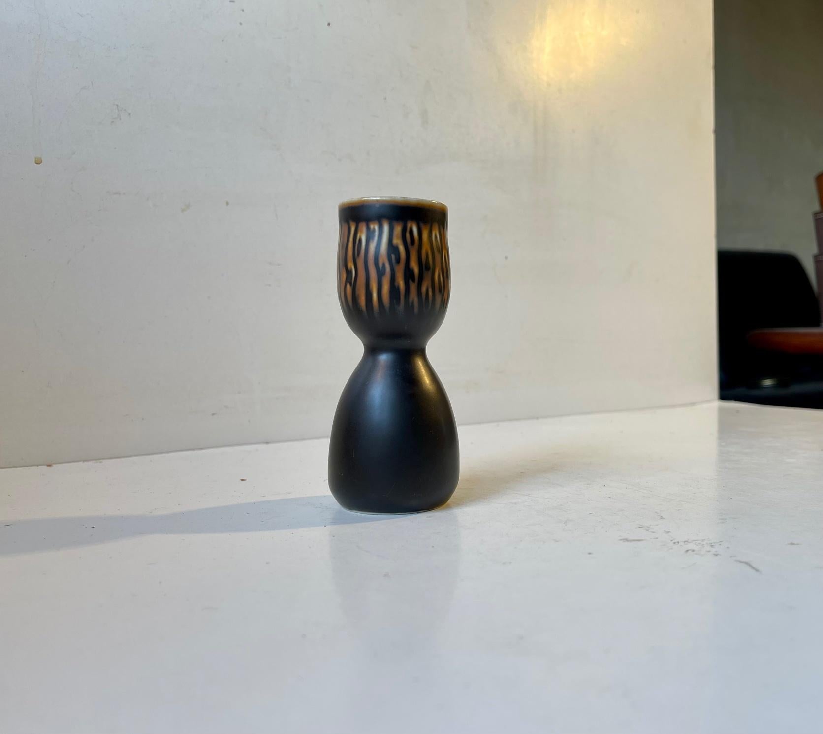 Axel Salto inspired piece from Royal Copenhagen. An hour glass shaped stoneware vase or candlestick designed by Gerd Bogelund during the 1950s or early 60s. Its decorated with a dark brown almost black main glaze and featuring abstract/floral