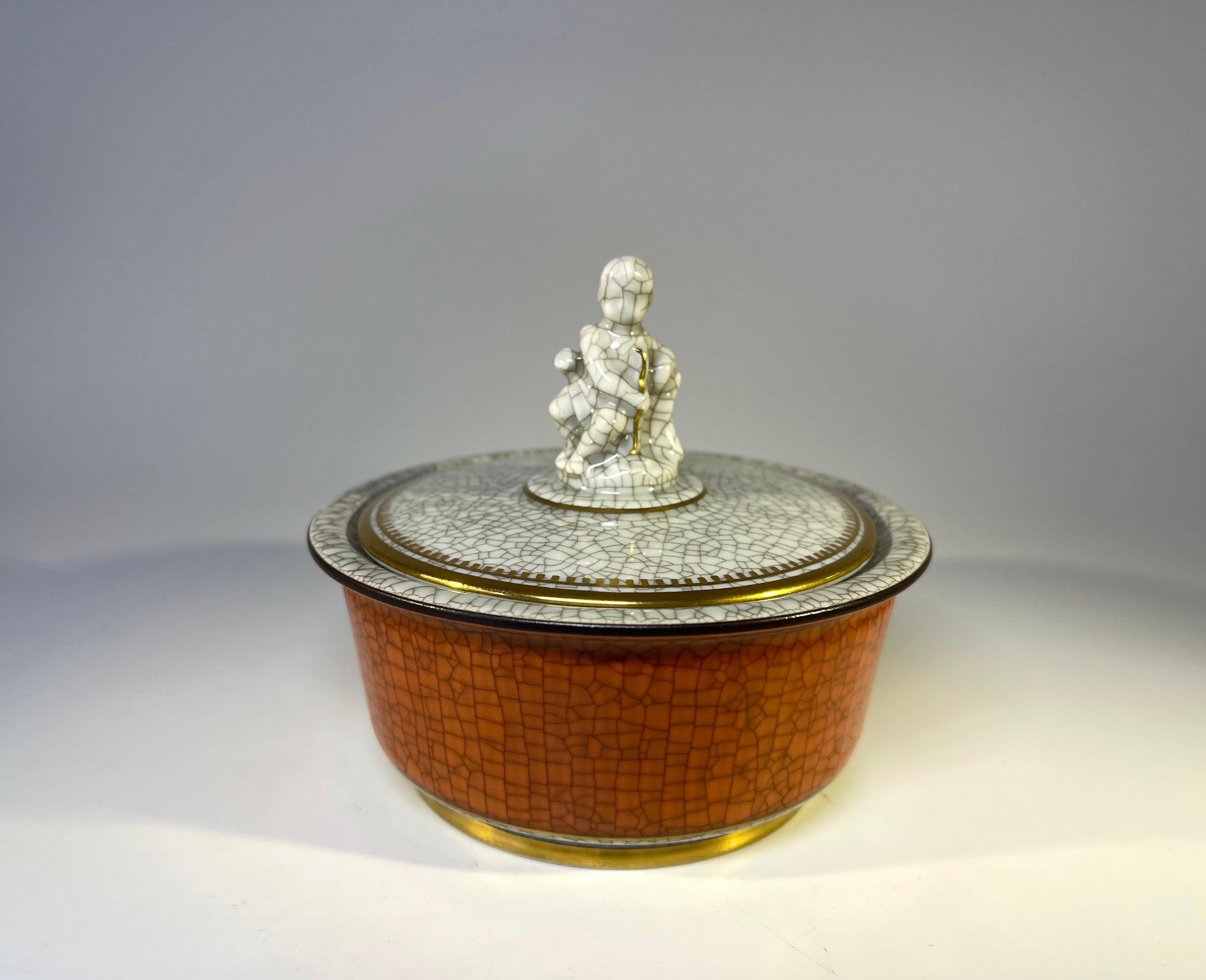 Royal Copenhagen terracotta crackle glaze pot with grey crackle glaze lid adorned with figural Cupid.
Decorated with gilt banding. 
Signed and numbered 2936
Circa 1954
Height 3.5 inch, Diameter 4.25 inch
In excellent condition. 
