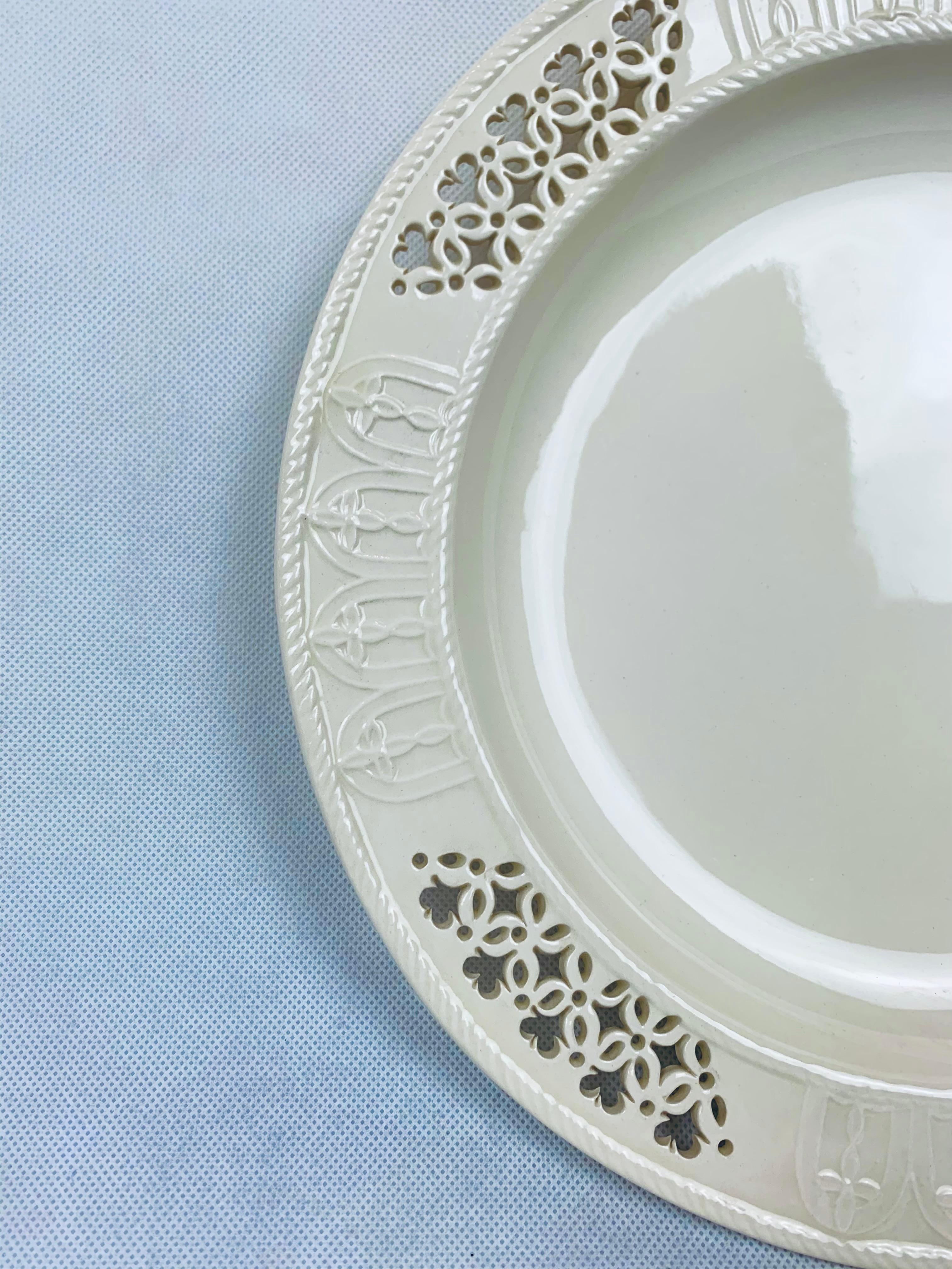 This Royal Creamware charger has a diameter of 12 1/4”.  There is a wide border of four reticulated sections and four in relief.  The center is plain and dished out.  This creamy glaze continues to be popular for over 200 years.  
The Royal