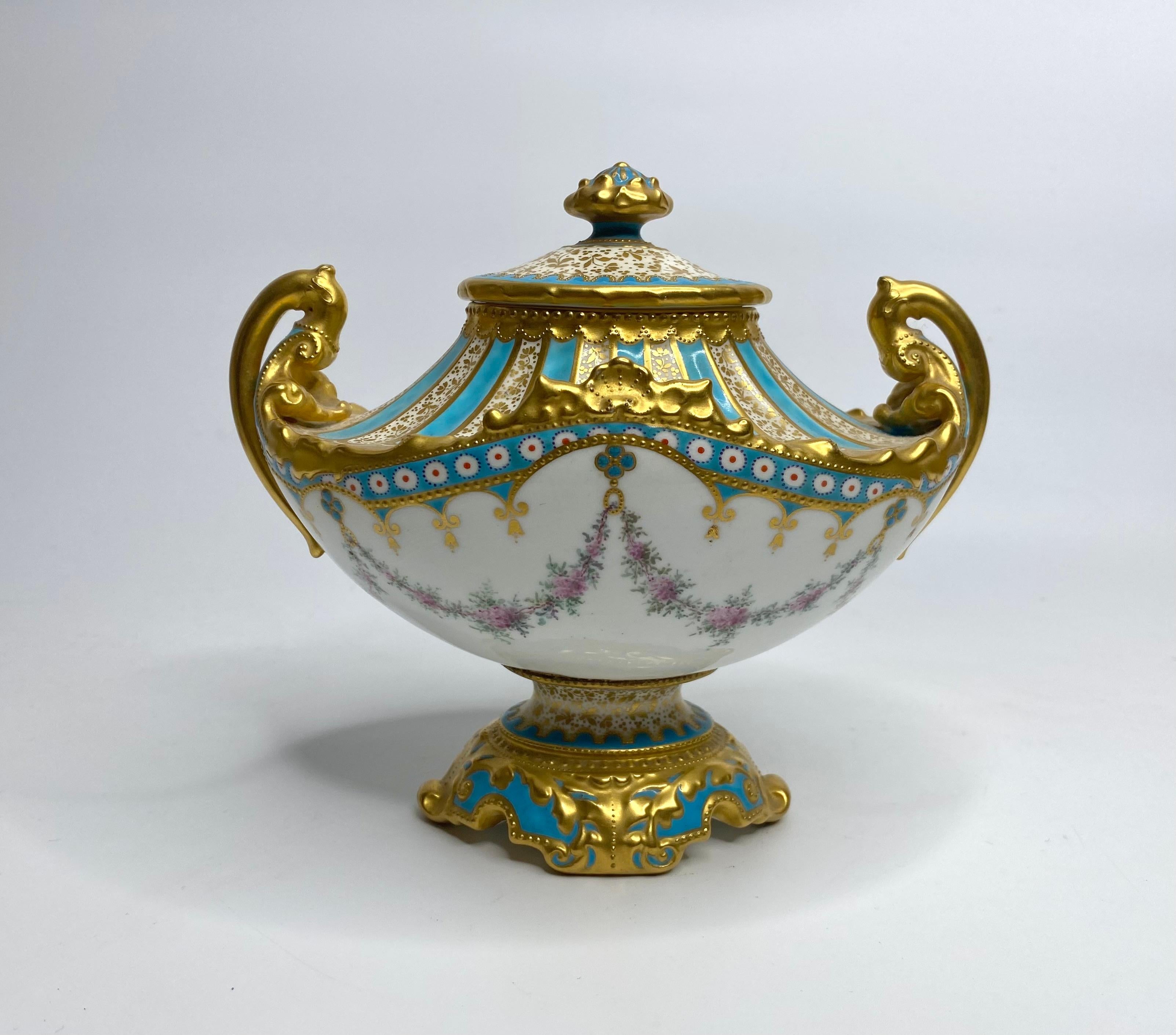 Royal Crown Derby Porzellanvase und Deckel, gemalt von Desire LeRoy, datiert 1897. Vase mit zwei Henkeln im Sèvres-Stil, handbemalt mit Blumenranken, die an einer Vase mit Blumen hängen, die durch blaue Blumenfelder unterteilt sind. 
Die Schulter
