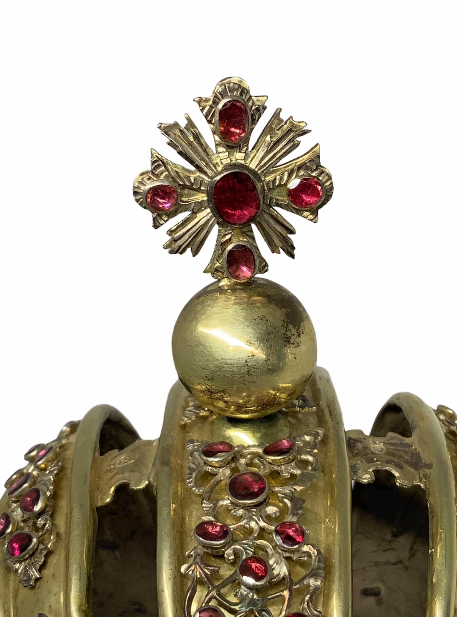 This gilt silver crown is made by three wide bands. These are embellished by silver festoons ornaments formed by scrolls and shells. Garnet stones bezel are scattered over them. There is a cross over a globe in the middle band that is also adorned