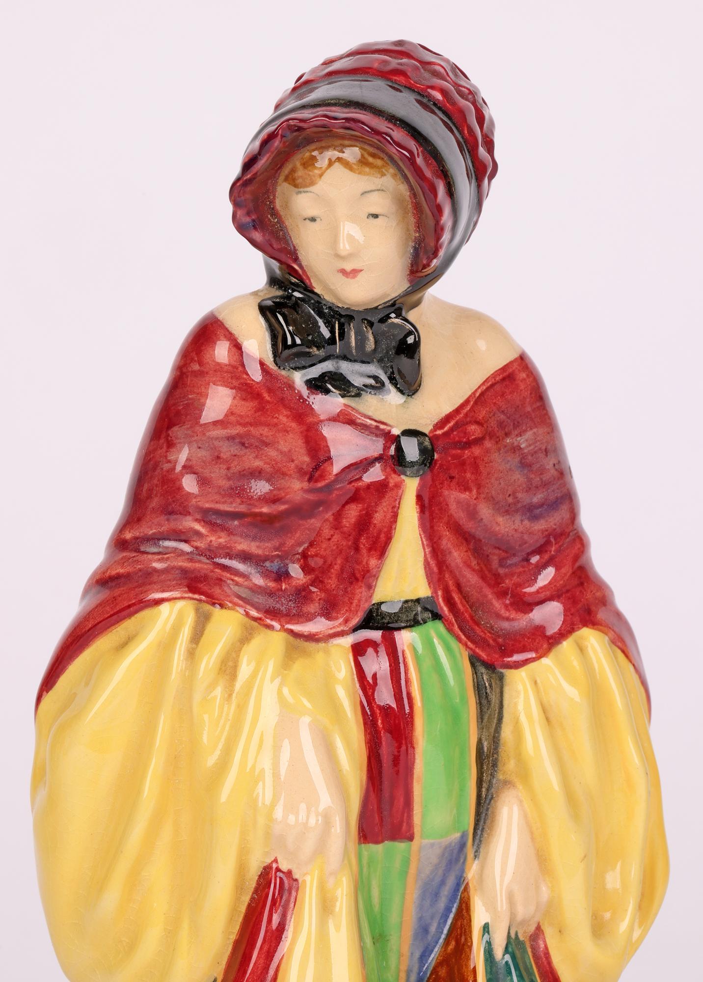 A fine and stylish Art Deco early figurine by Royal Doulton titled The Parsons Daughter and designed by Harry Tittensor and dating between 1929 and 1938. The lightly potted hollow figurine wears a short cape fastened at the front over a full length