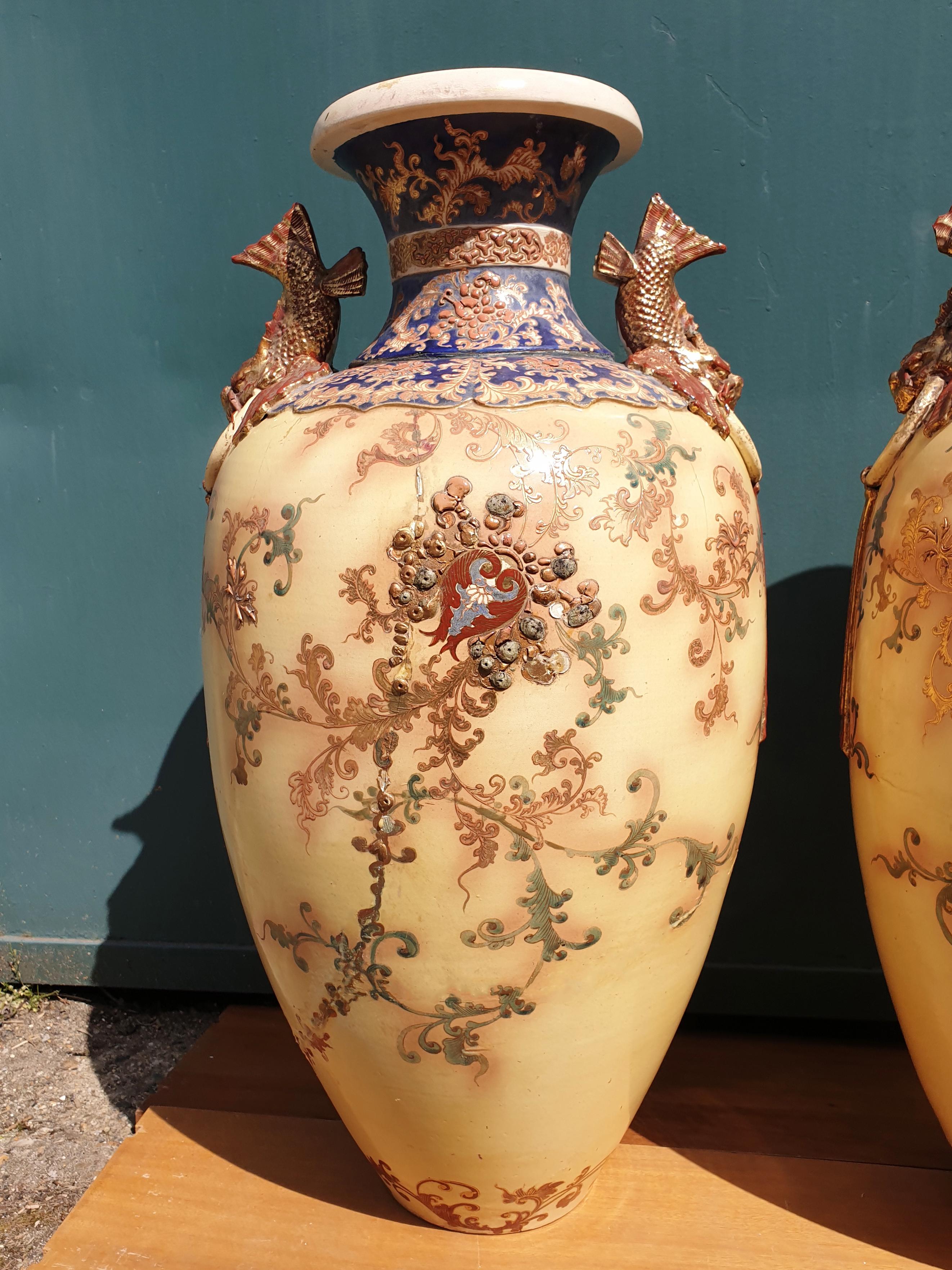 An impressive pair of Royal Doulton fish handle vases that presents in an oval form with a short waisted neck and turned out rims. The main body of the vases are decorated with trailing leaves and vines with some porcelain jewelling. The neck