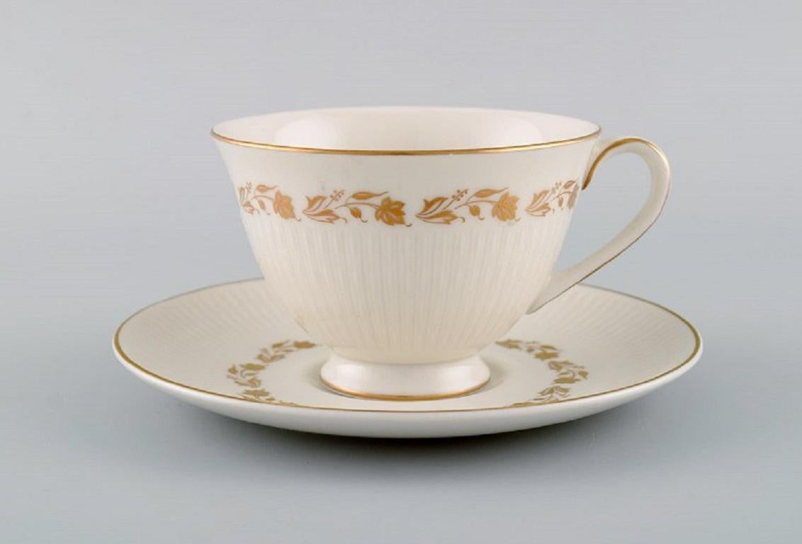 Royal Doulton, England. Twelve Fairfax teacups with saucers and a cream jug in porcelain with hand-painted flowers in gold. 
Mid-20th century.
The cup measures: 10 x 6.7 cm.
Saucer diameter: 15.7 cm.
The cream jug measures: 13 x 9.5 cm.
In