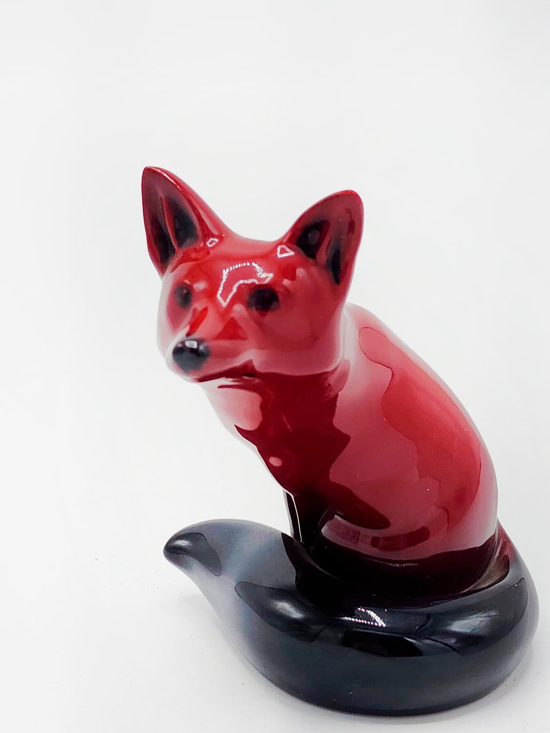 This adorable Figurine is made out of bone china / porcelain. This lovely little piece was issued by Royal Doulton in 1913-1962 and is a part of the flambe style collection, which uses a copper oxide glaze for the deep red finish. The sculpture is a