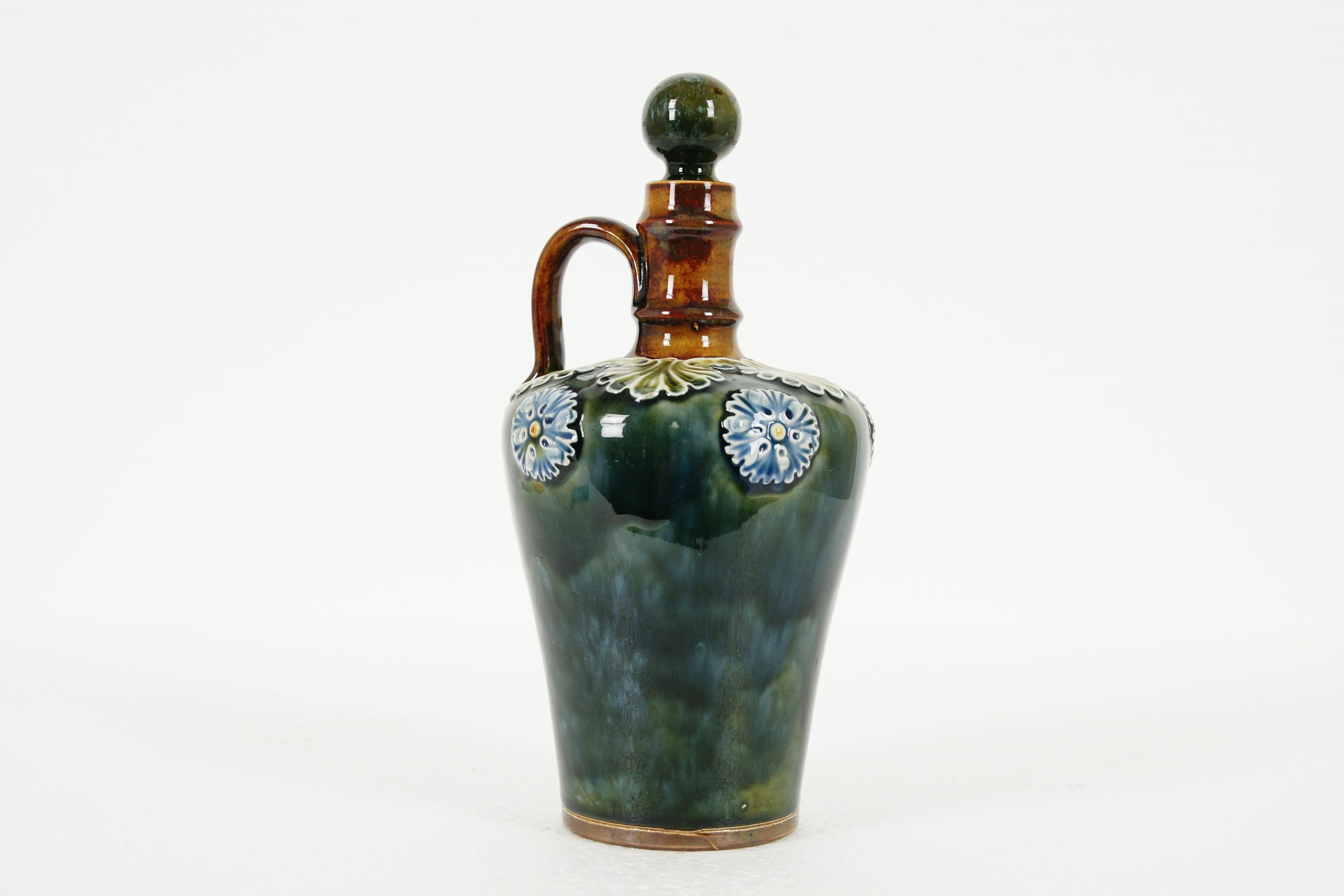 Royal Doulton, Lambeth stoneware flagon, decanter, whisky bottle with stopper, B1970

Lovely flash shape
Green and blue glaze
Decorated with flowers and leaves
Lovely shaped handle to the top
Base is stained with design
Number 689, 213
In