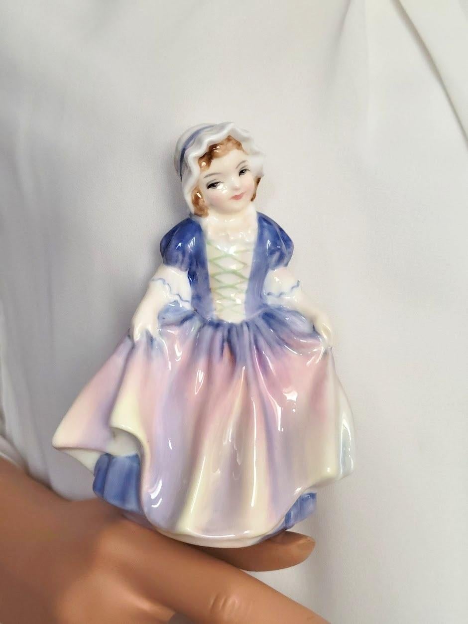 A lovely miniature vintage porcelain figurine Royal Doulton “Dinky Do,” HN 1678, decorated in a light purple and pink colorway, was designed by leading Doulton artist Leslie Harradine in the “Harradine – Child Classics” Series.

The size of the