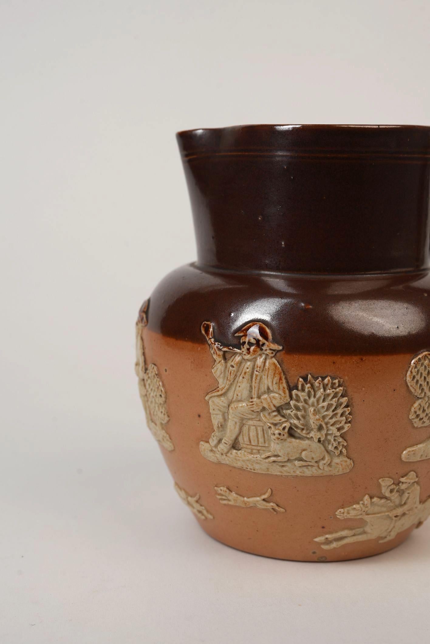 This striking Royal Doulton stoneware jug is a fine example of early 20th-century British ceramic artistry, crafted circa 1905 during the Edwardian era. Its two-tone glaze—rich chocolate brown upper and a natural buff lower body—creates an elegant