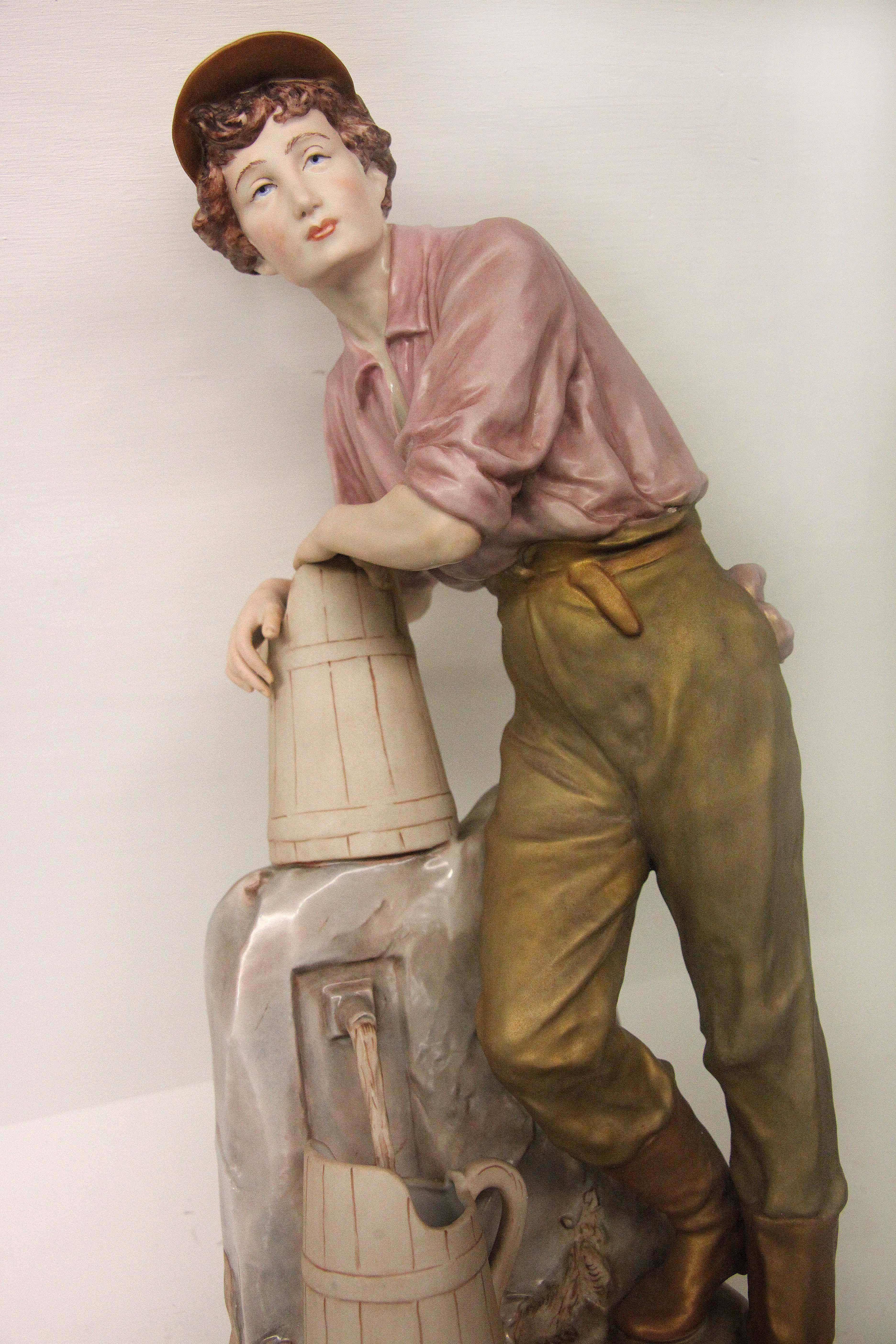 Royal Dux pheasant boy figurine, early 20th century, standing at the well filling jugs with water.
