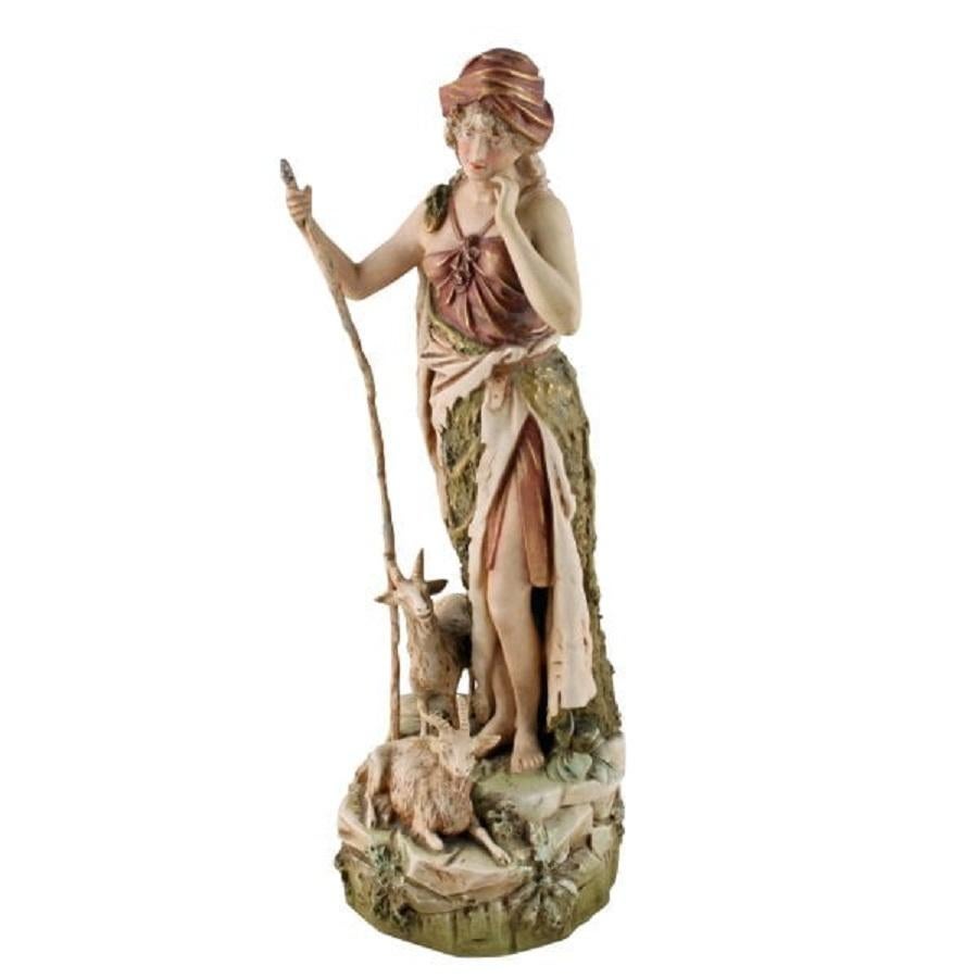 A late 19th century Bohemian Royal Dux porcelain figure of a goat herder.

The female figure is dressed in middle eastern attire and is resting on her staff with two goats at her feet.

The model is set in a natural landscape with the figure