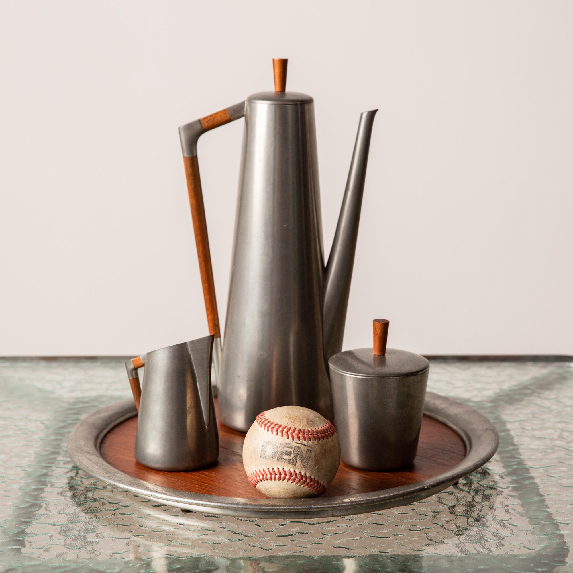 A Royal Holland four-piece service set in pewter with teak handles and accents, by J.N. Daalderop & Sons. This Royal Netherlands Metalworks set consists of one lidded pot used for coffee or tea, one creamer, one lidded sugar vessel, and a serving