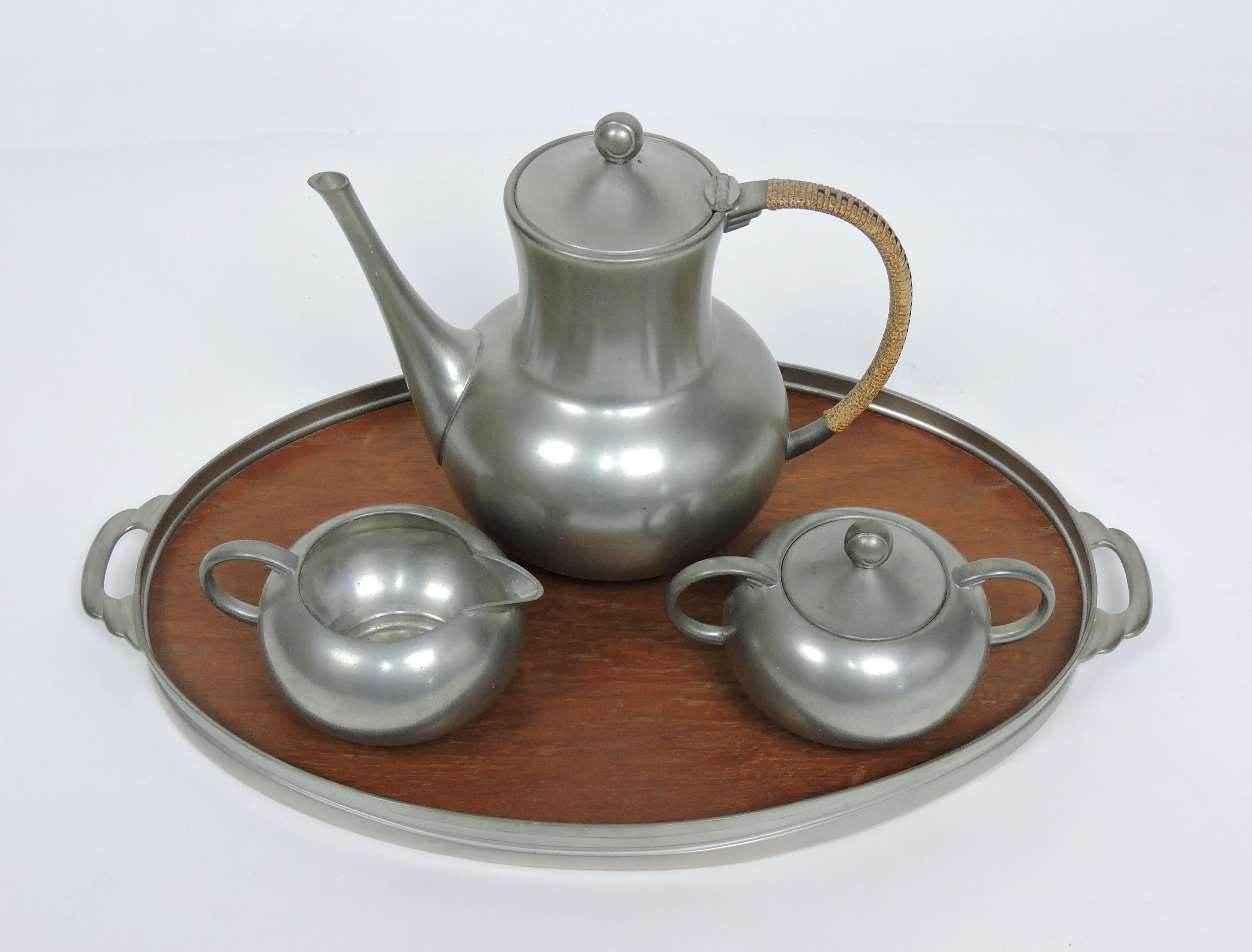 Beautiful Mid Century pewter coffee set made by Royal Holland in the Netherlands. This set includes a lidded coffee pot with a rattan wrapped handle, a lidded sugar bowl, a creamer, and a tray with a teak insert. Marked on bottom.

